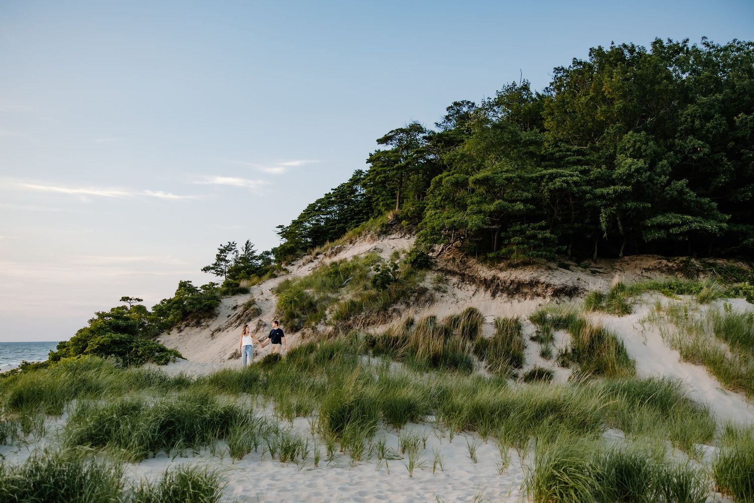 Sandy dunes covered in beach grass stretch along the coastline under a bright blue sky.