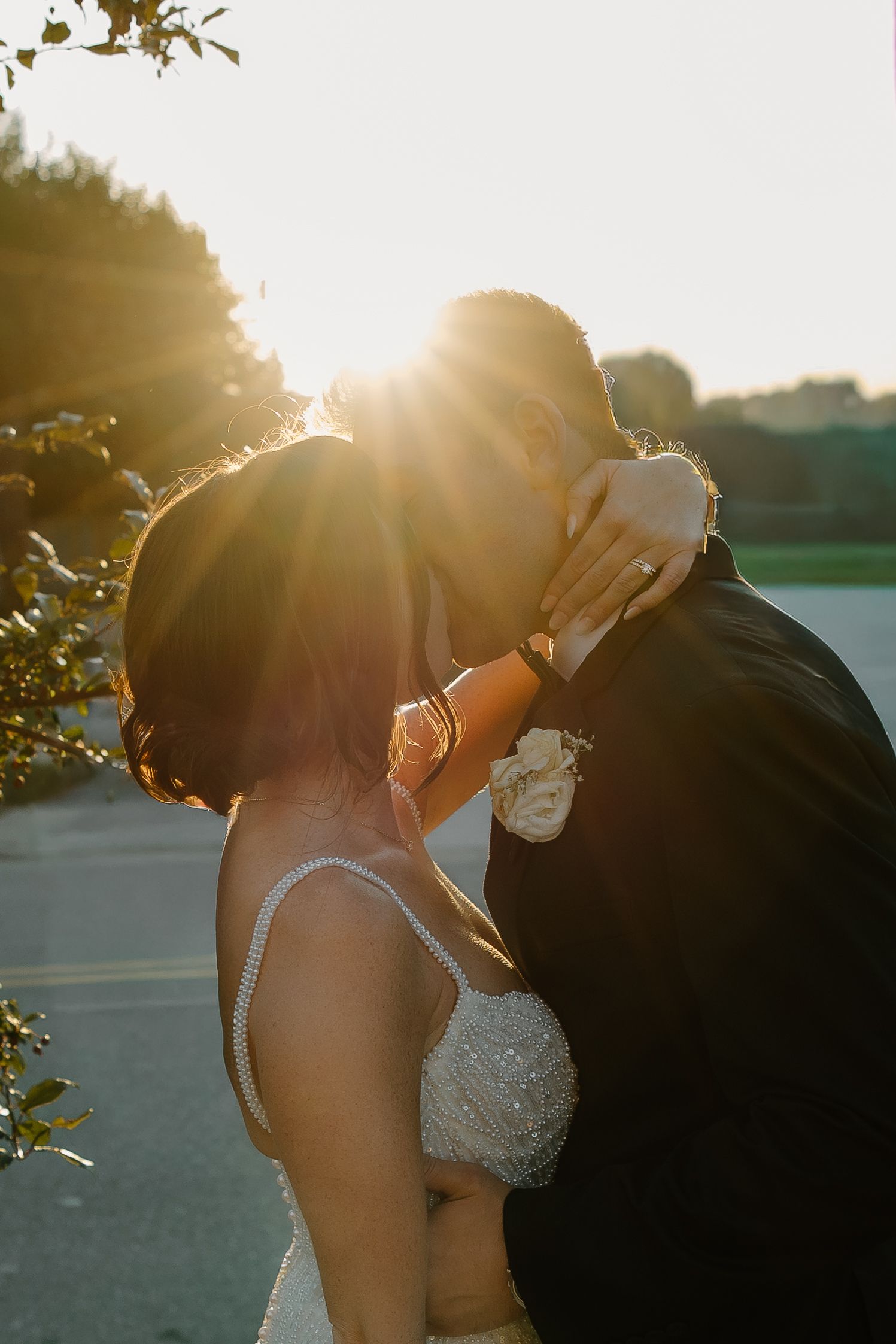 Intimate sunset kiss between newlyweds with golden sunlight streaming through trees.
