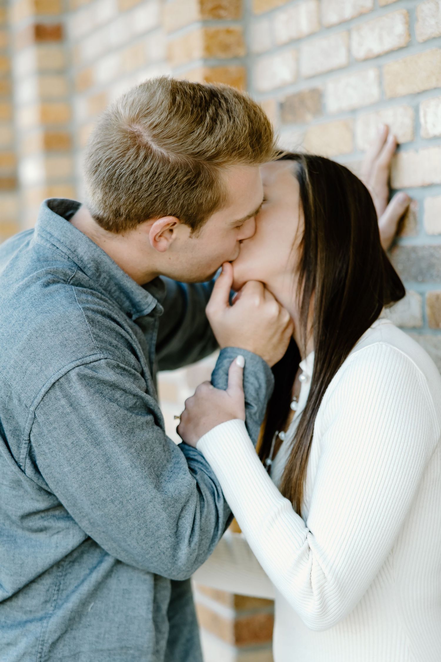 Intimate moment captured against textured brick wall background.