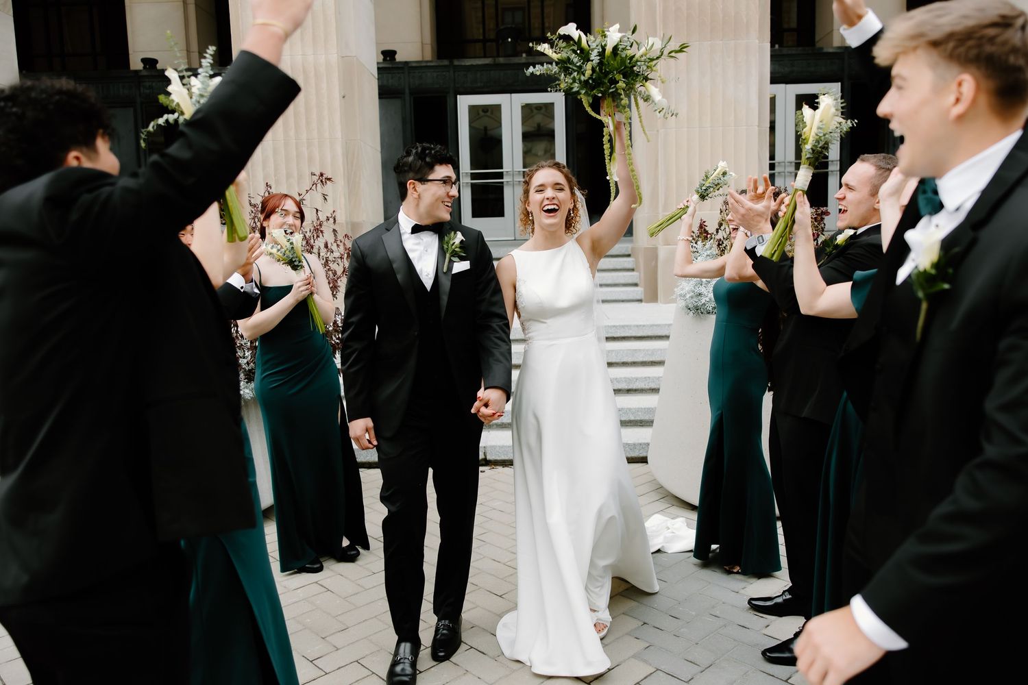 Joyful wedding celebration on stone steps with wedding party in emerald green and black attire.