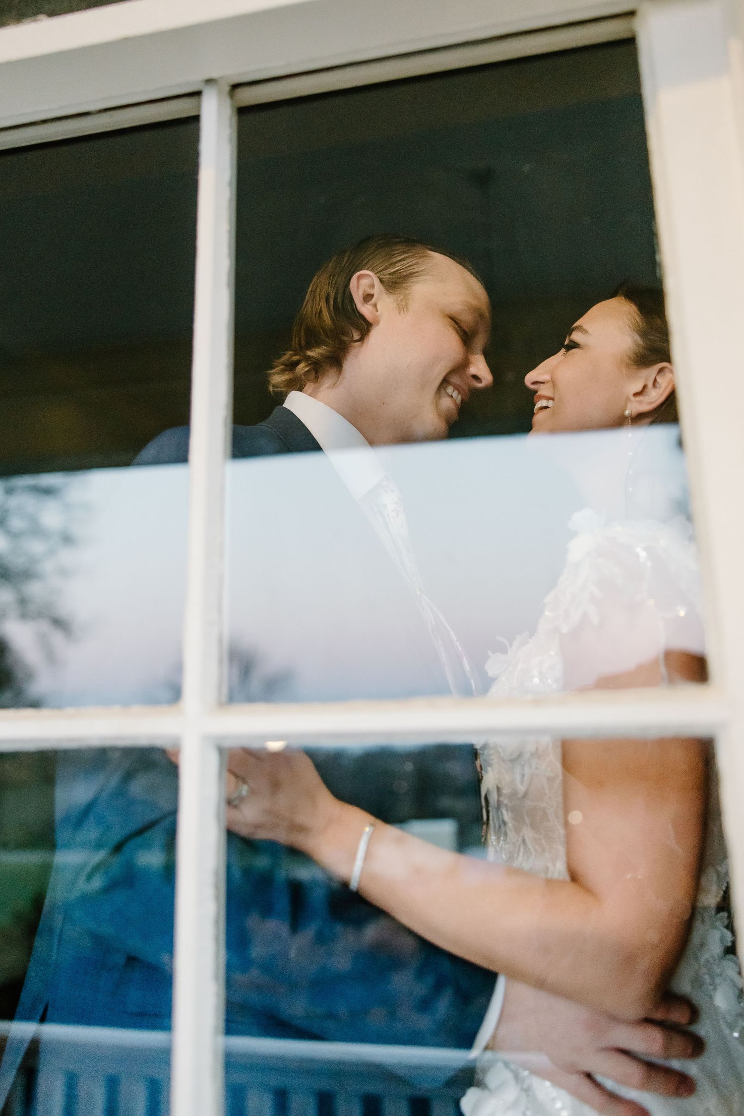 Romantic window reflections capture tender wedding moments through windowpanes.