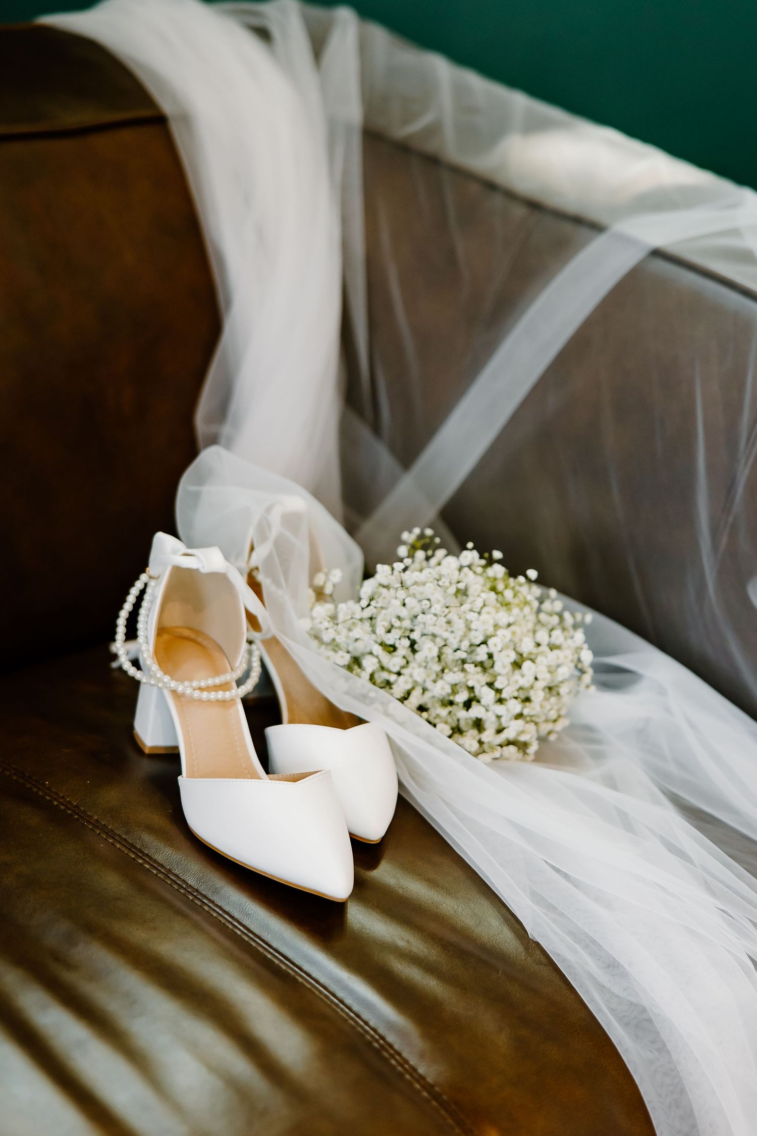 White bridal shoes with baby's breath flowers and veil on leather surface.