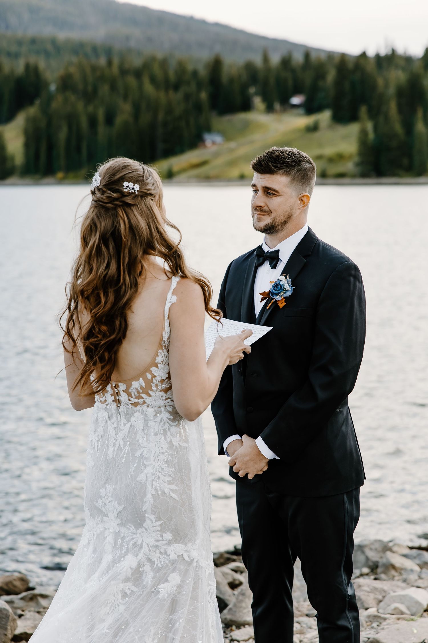 Emotional wedding vow exchange by a serene mountain lake with pine forests in the background.