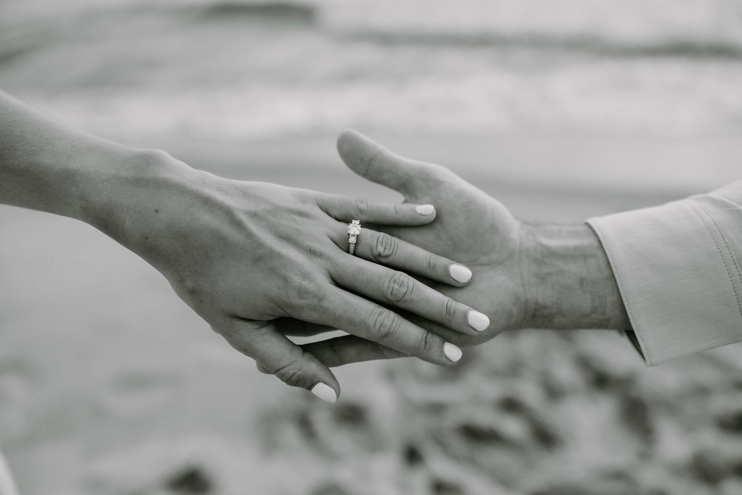 Black and white close-up of hands with engagement ring touching.