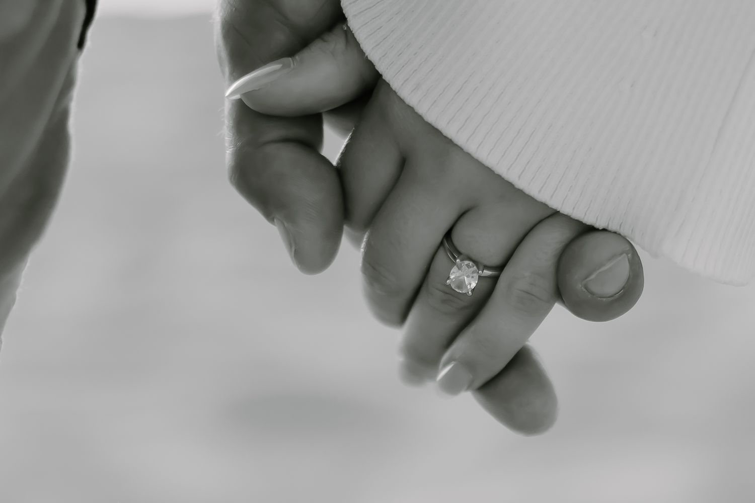Close-up of hands showing engagement ring against white background.