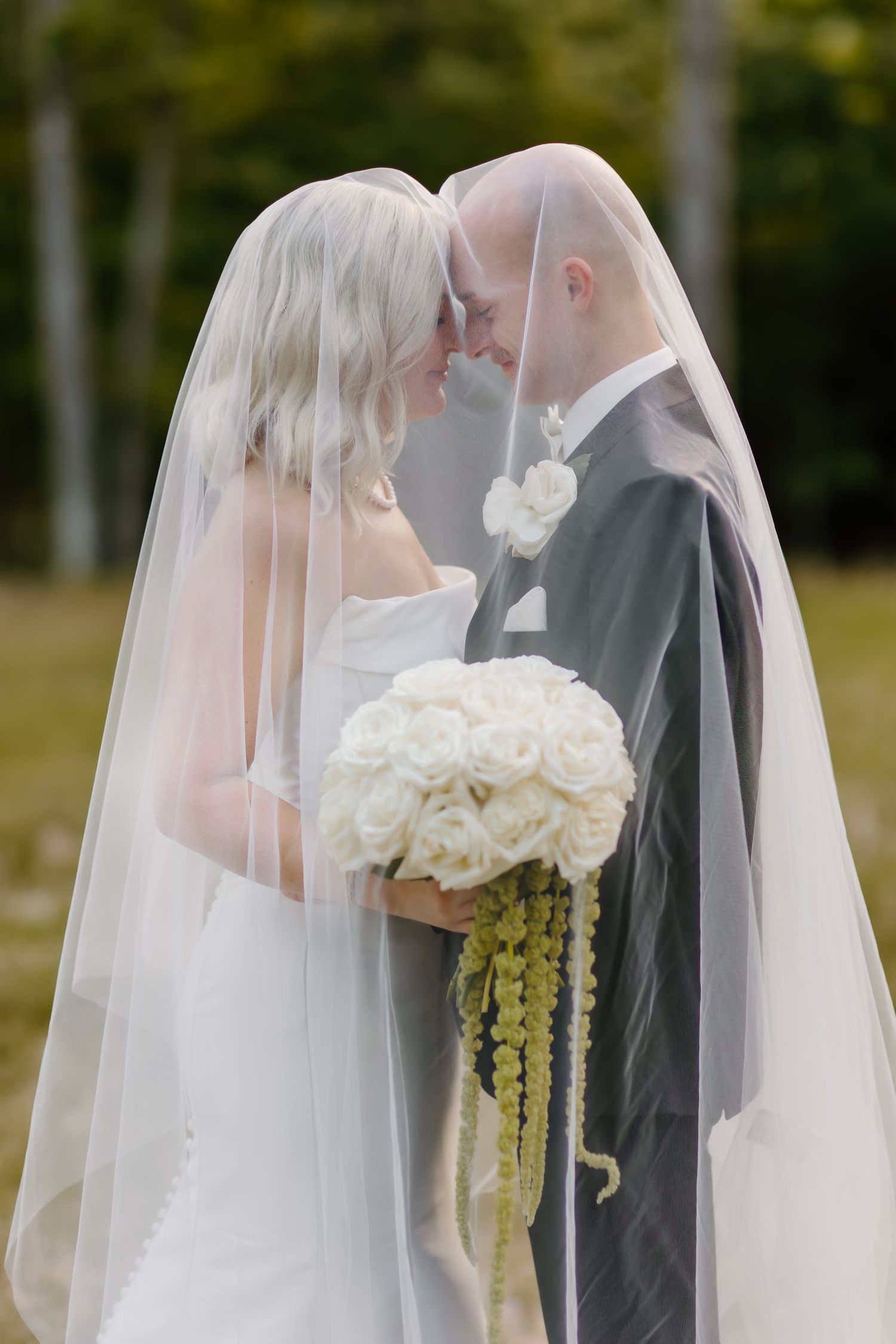 Romantic wedding couple sharing an intimate moment under a flowing white veil outdoors.