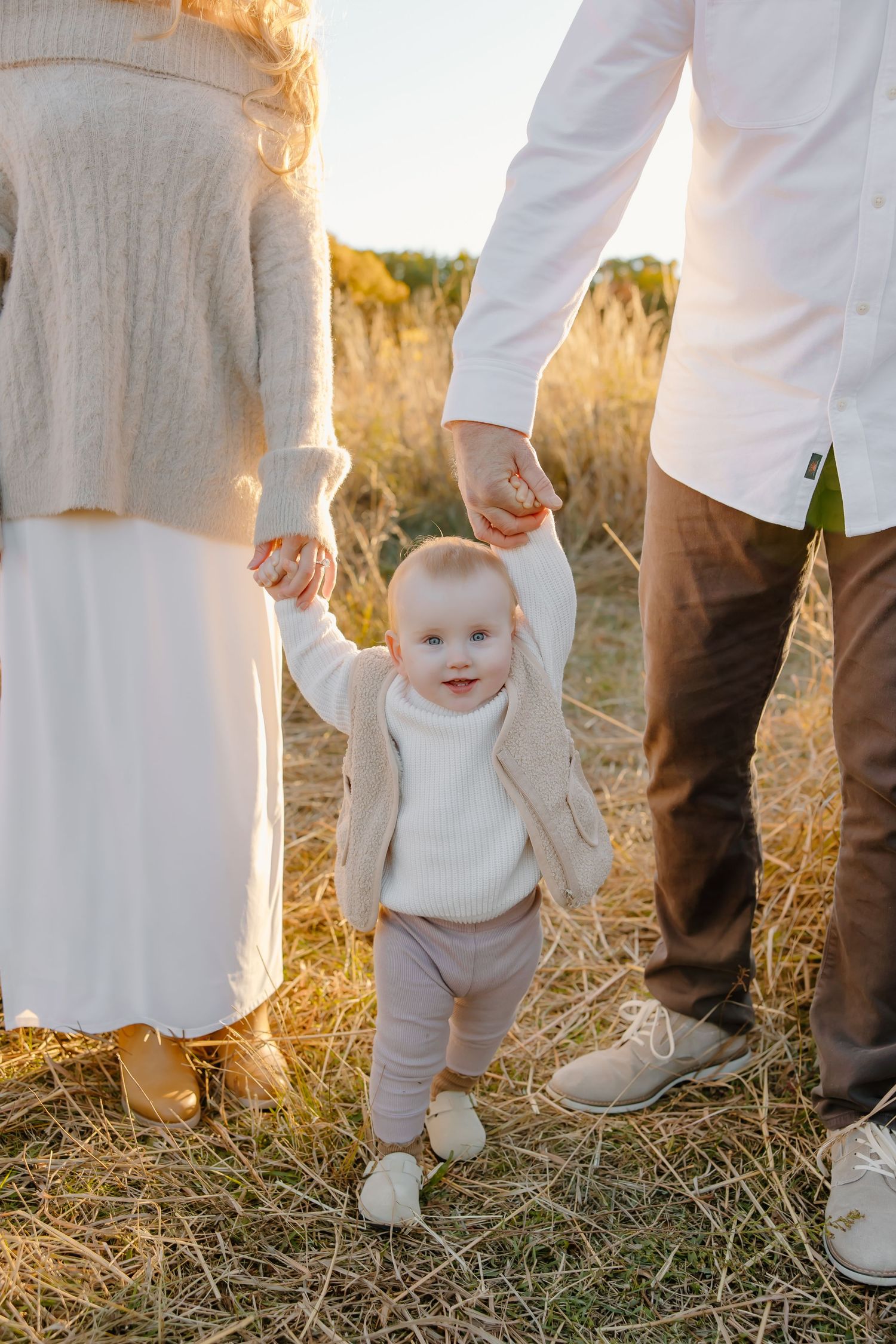 Family feet in white clothing standing together on autumn grass.