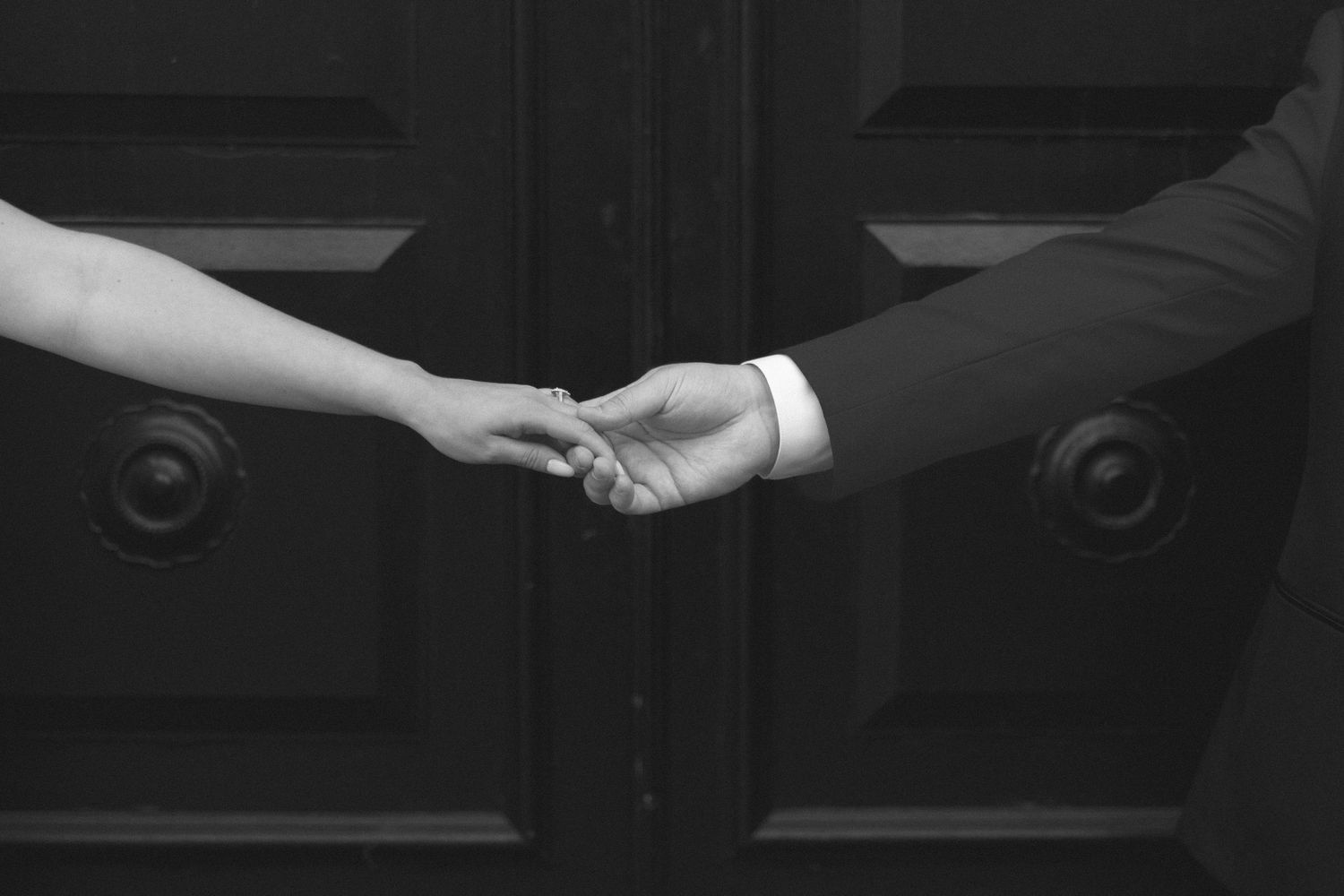 Black and white close-up of two hands clasped together against dark background.