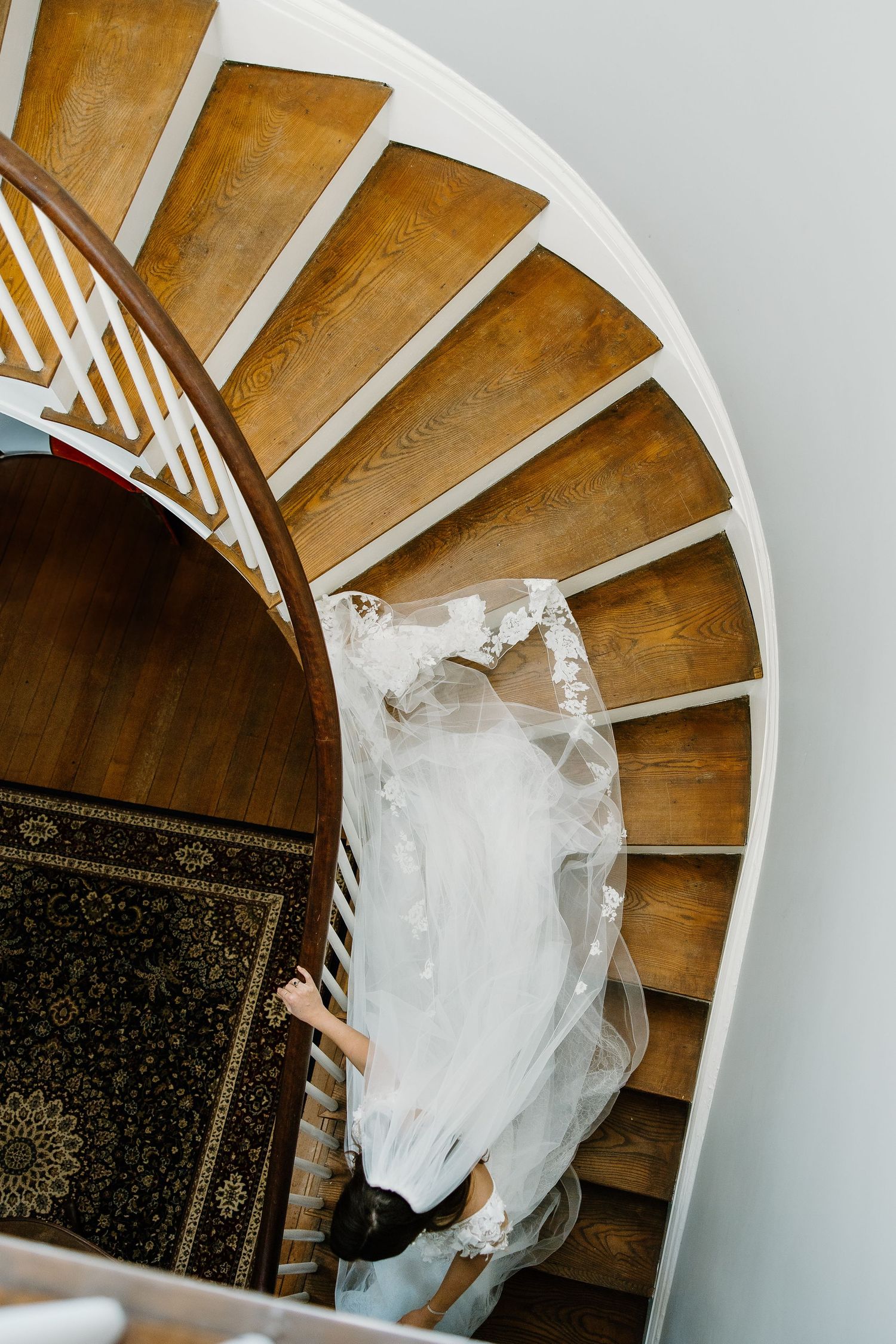 Bird's eye view of flowing wedding dress trailing down spiral wooden staircase.