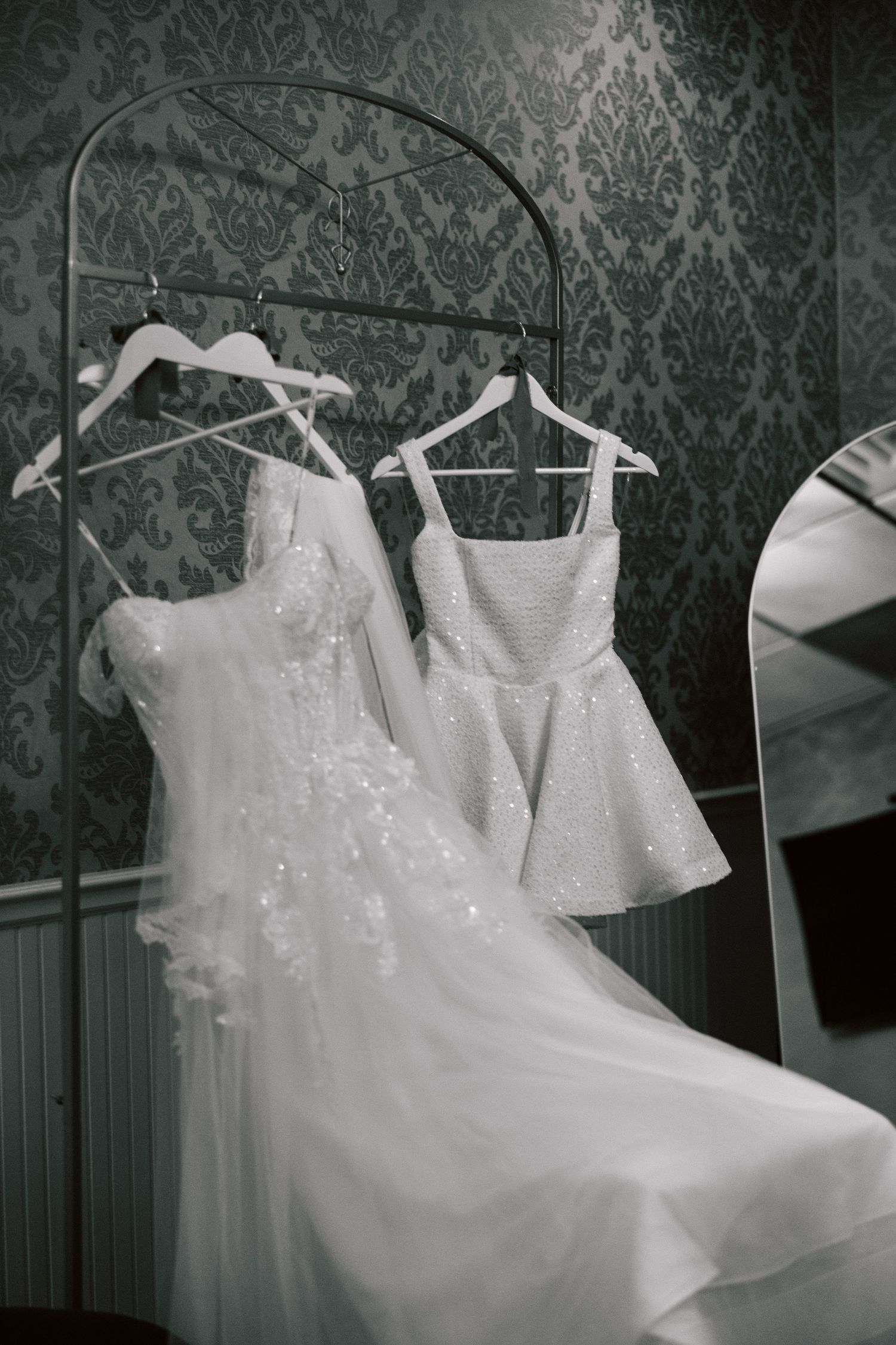 White wedding dresses hang on display against a dark patterned wallpaper background.