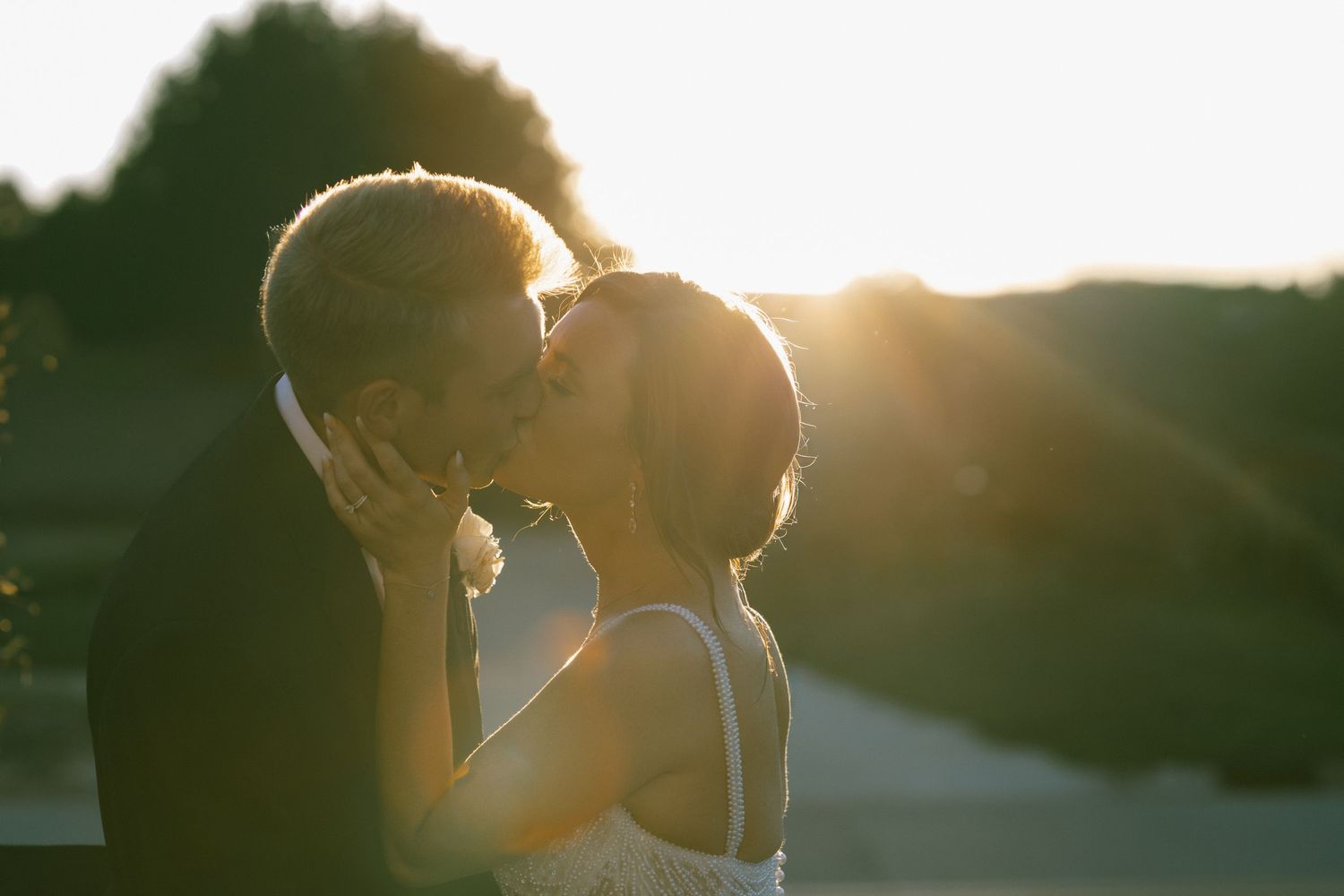 Sunset wedding portrait with couple embracing in golden backlight.