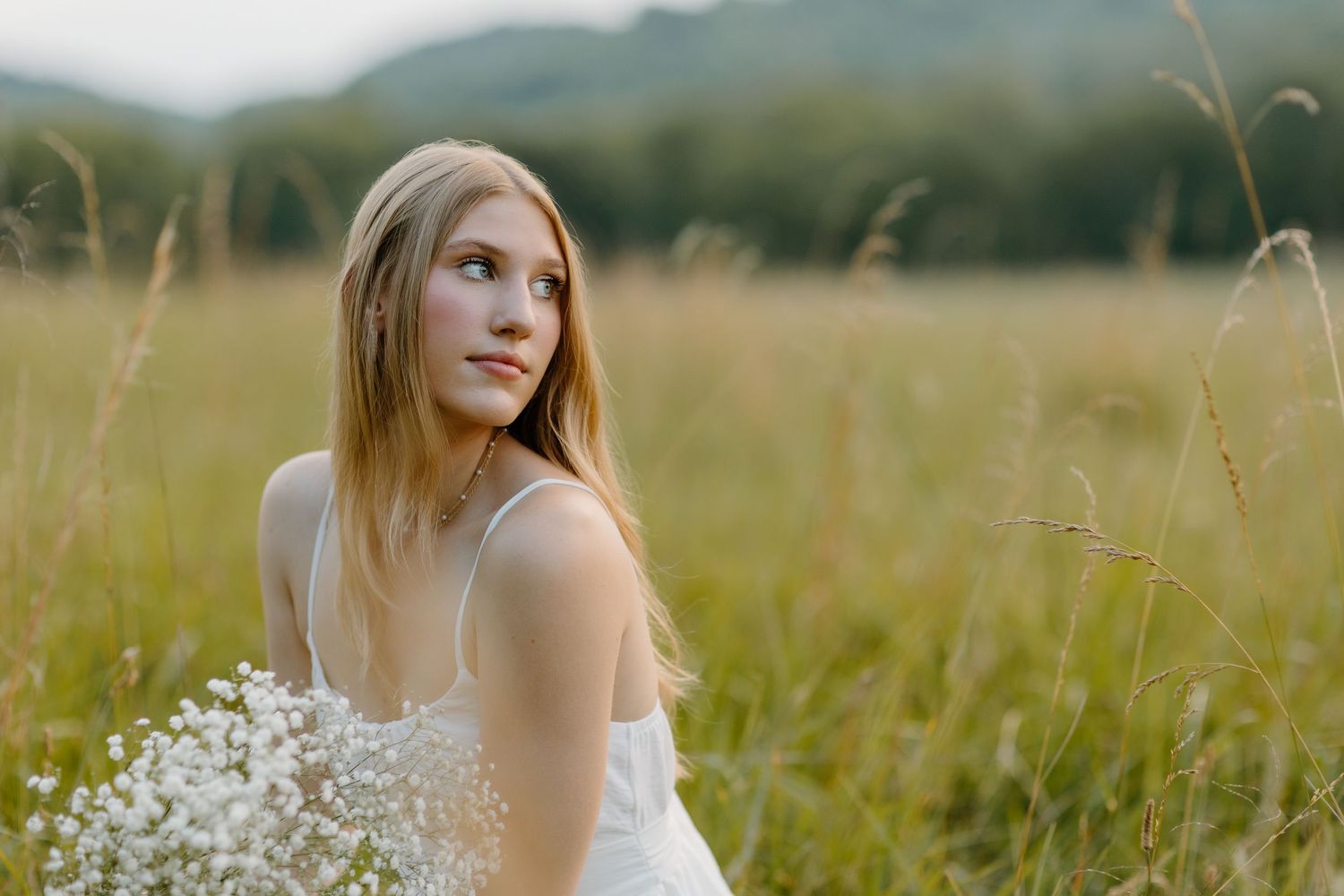 A dreamy portrait in a summer meadow with tall grass and delicate white wildflowers at golden hour.