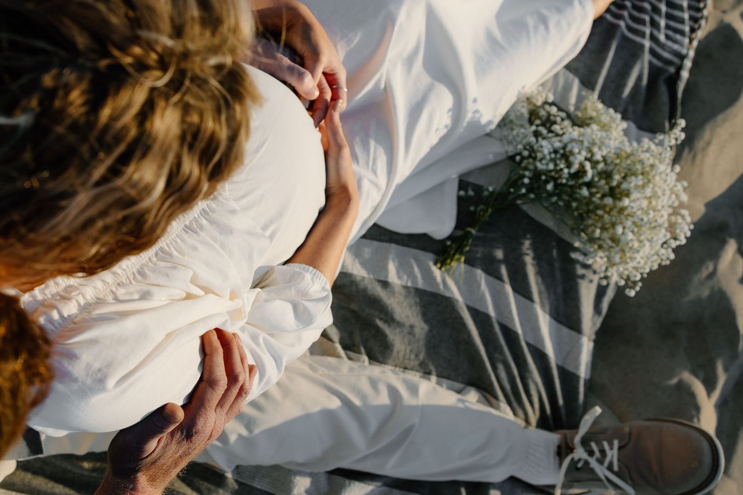 Close-up details of white dress and romantic moments on the beach sand.