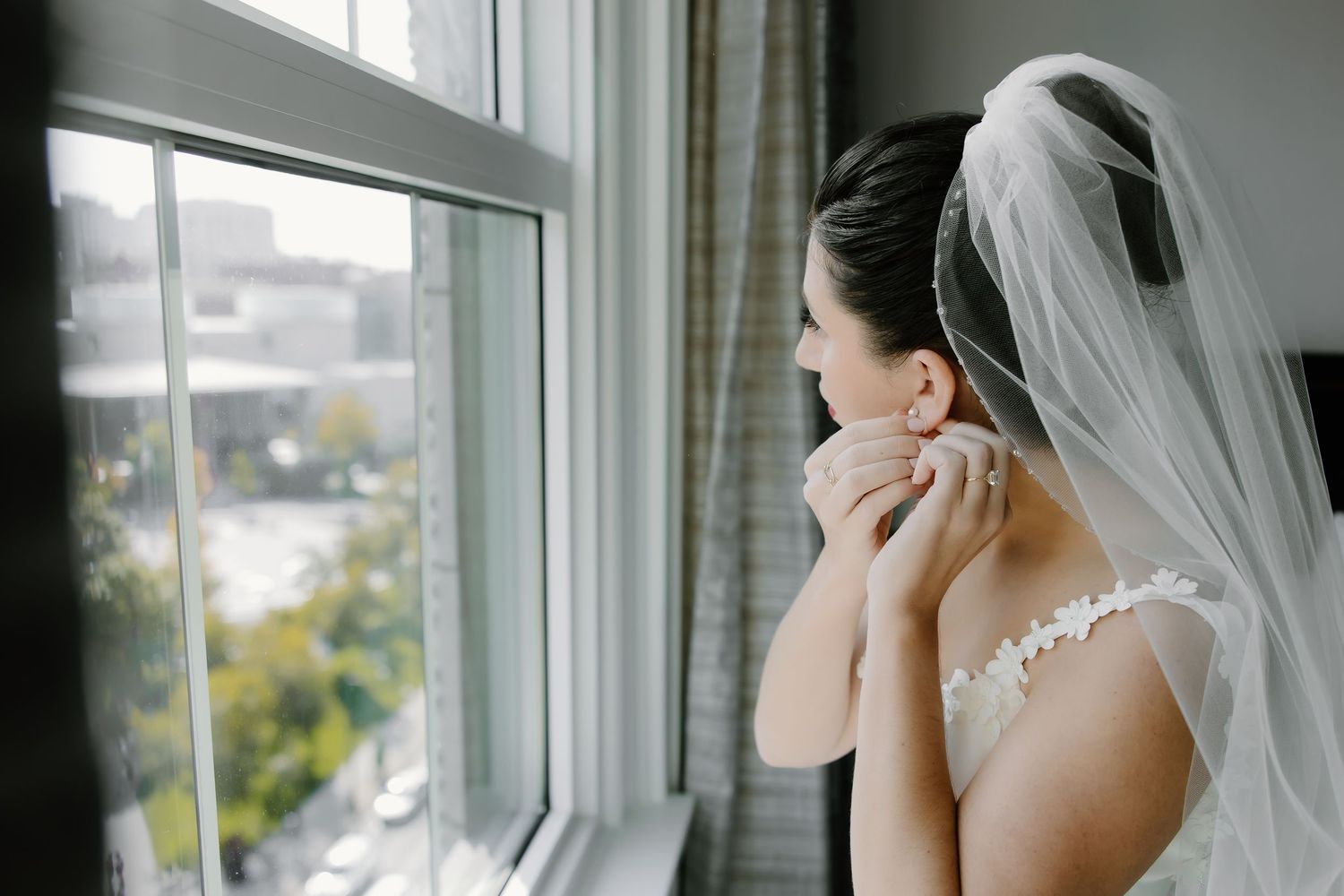 Elegant white wedding gown and veil details captured through window light in a getting ready room.