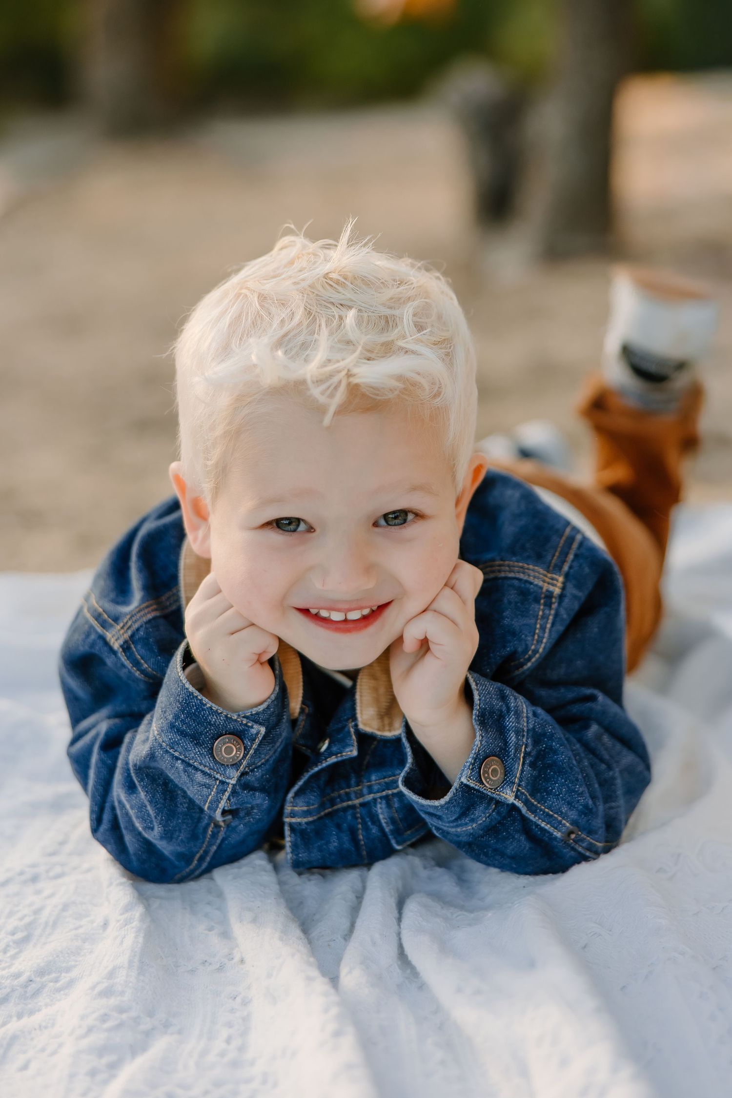 Child wearing denim jacket lying on white surface with joyful expressions.