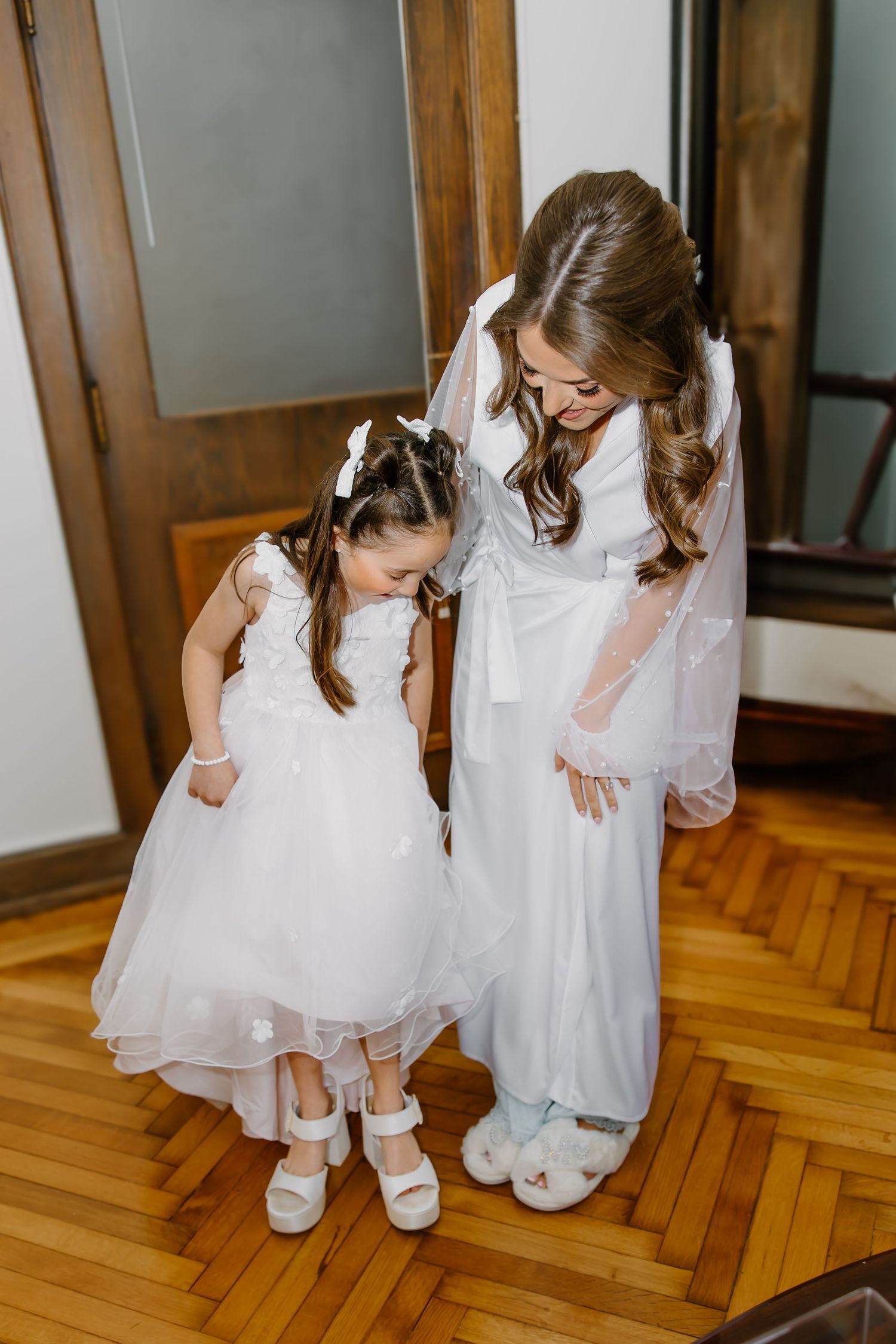 Young flower girls in white dresses playing on hardwood floors.