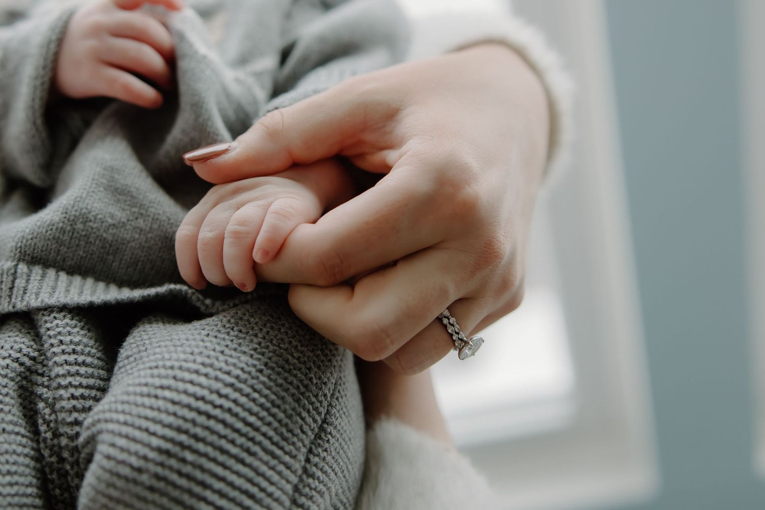 Close-up detail of hands wearing knit sweaters in soft, natural window light.