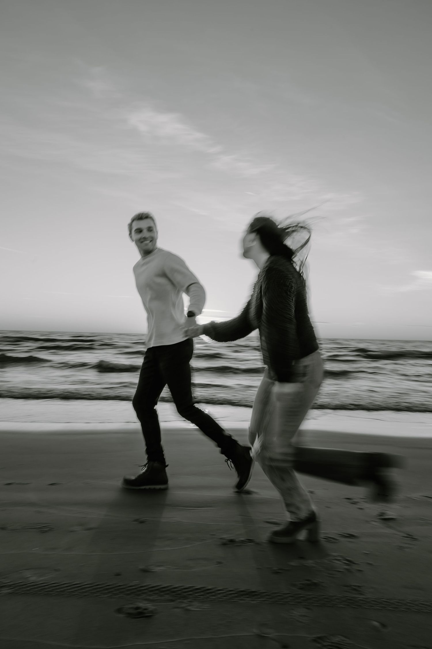 Black and white photo of two people dancing on a beach with artistic motion blur.