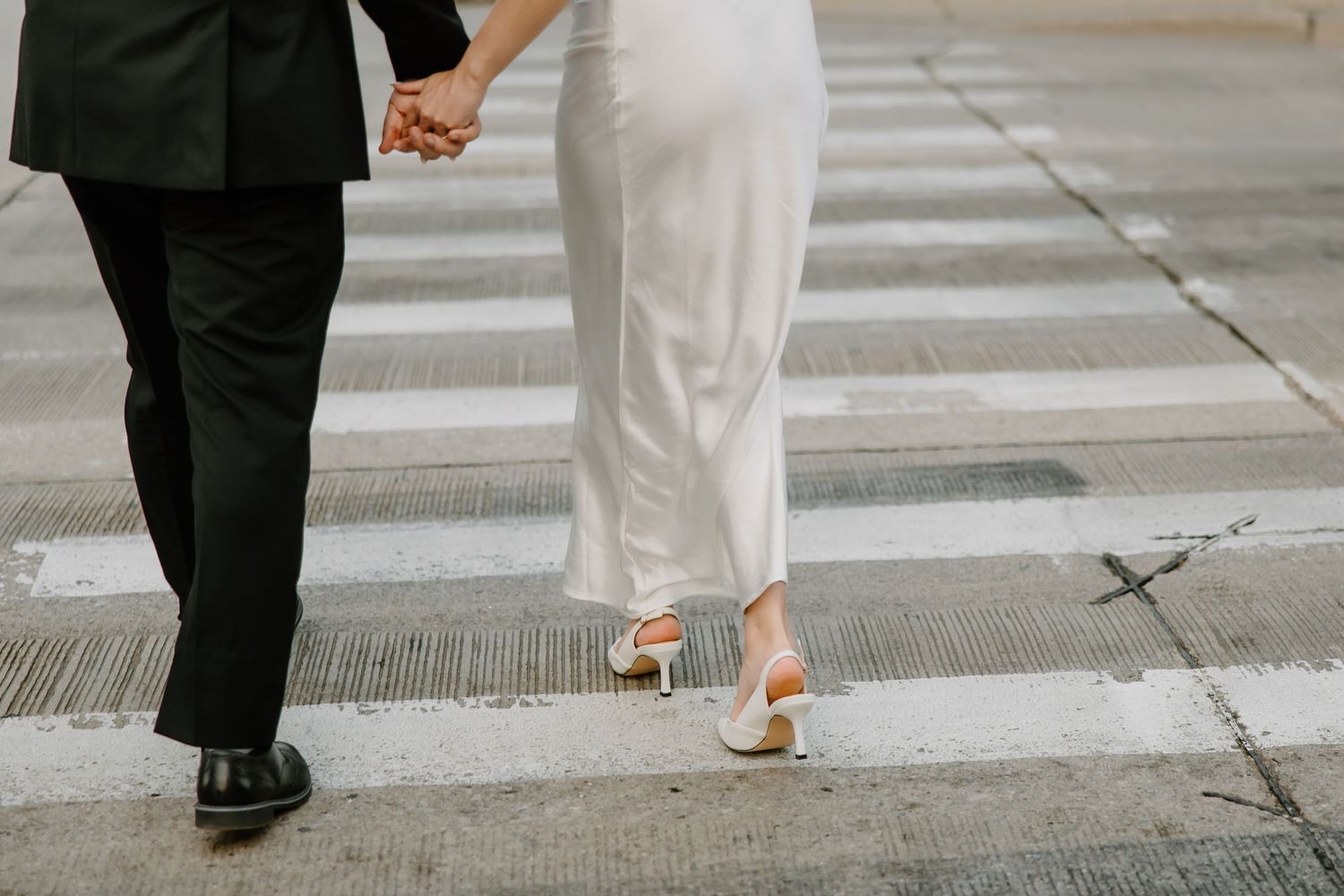 Wedding couple's feet walking together on urban sidewalk.