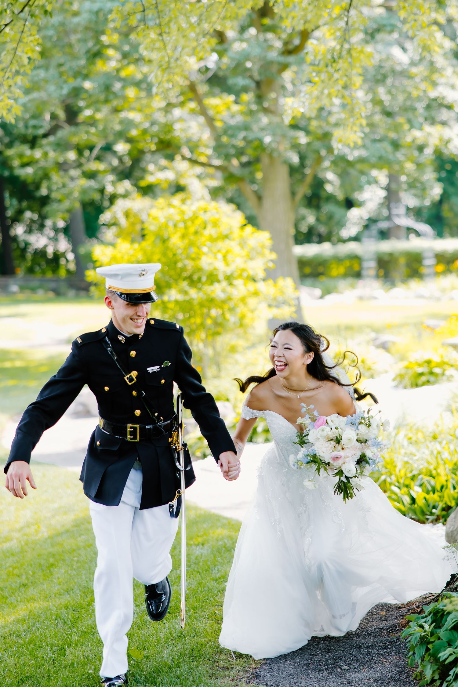 Military wedding couple running playfully through a sunlit garden.