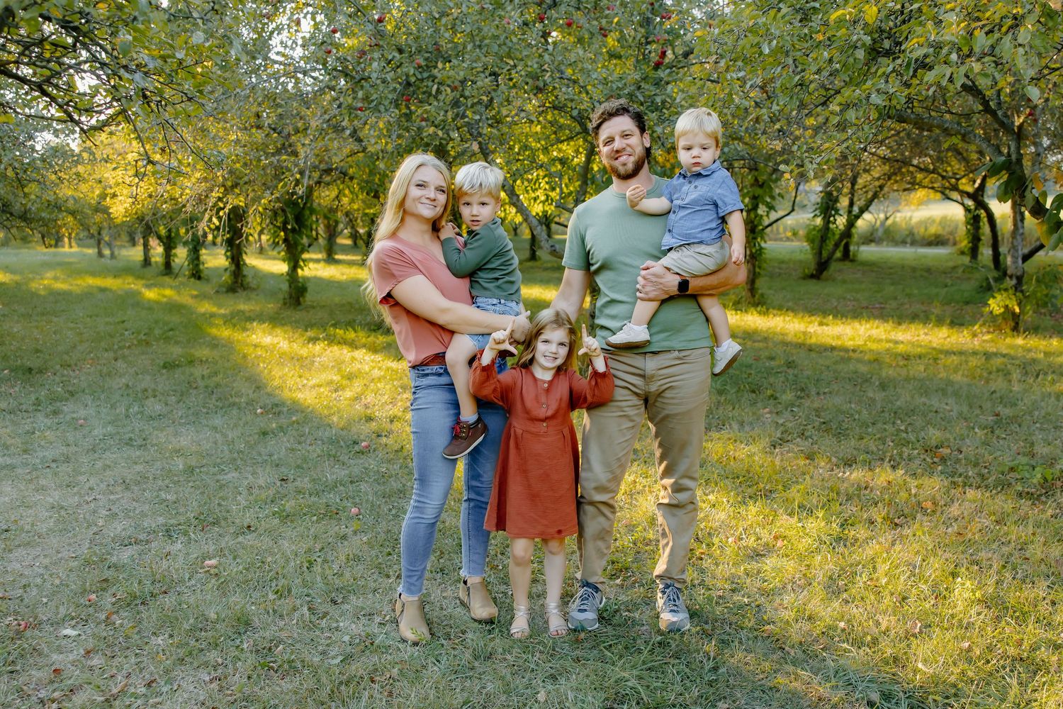 Family of five poses together in an orchard during golden sunset light.