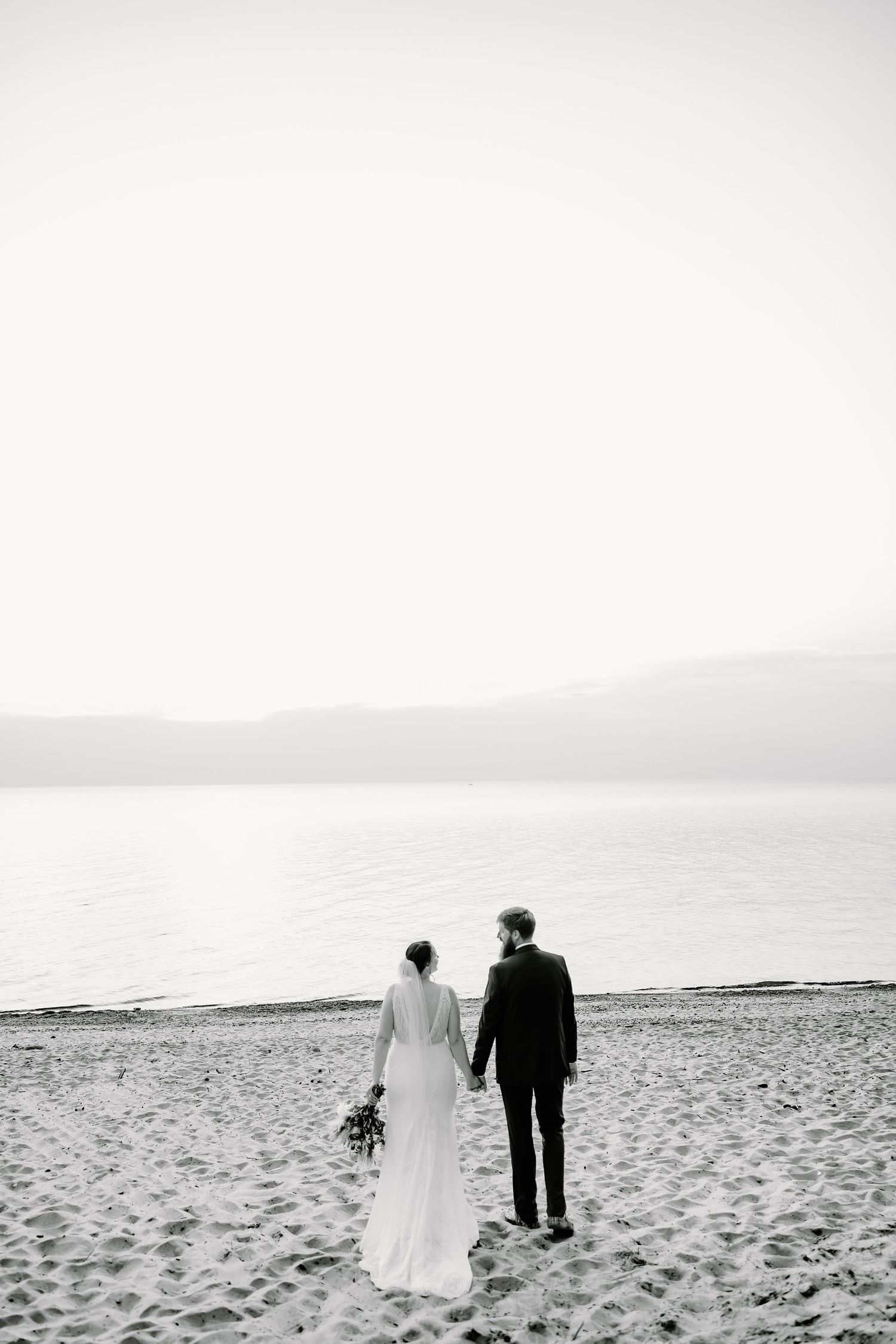 Serene beach wedding photos with couple walking along misty shoreline.
