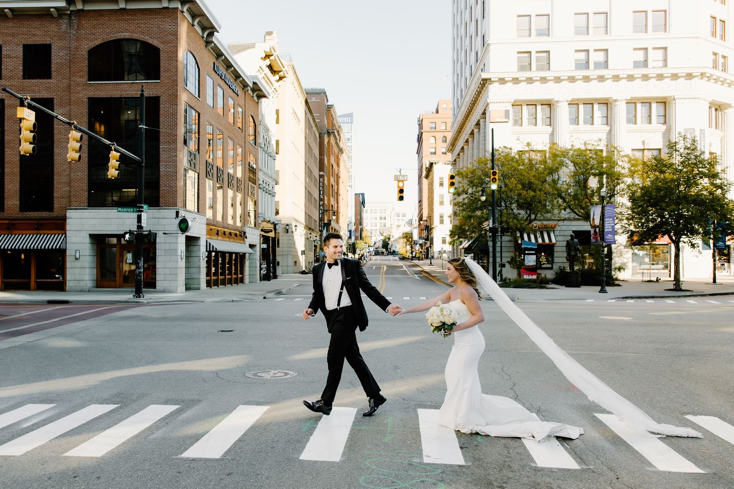 Wedding couple walks across a city crosswalk during a photo session at sunset.