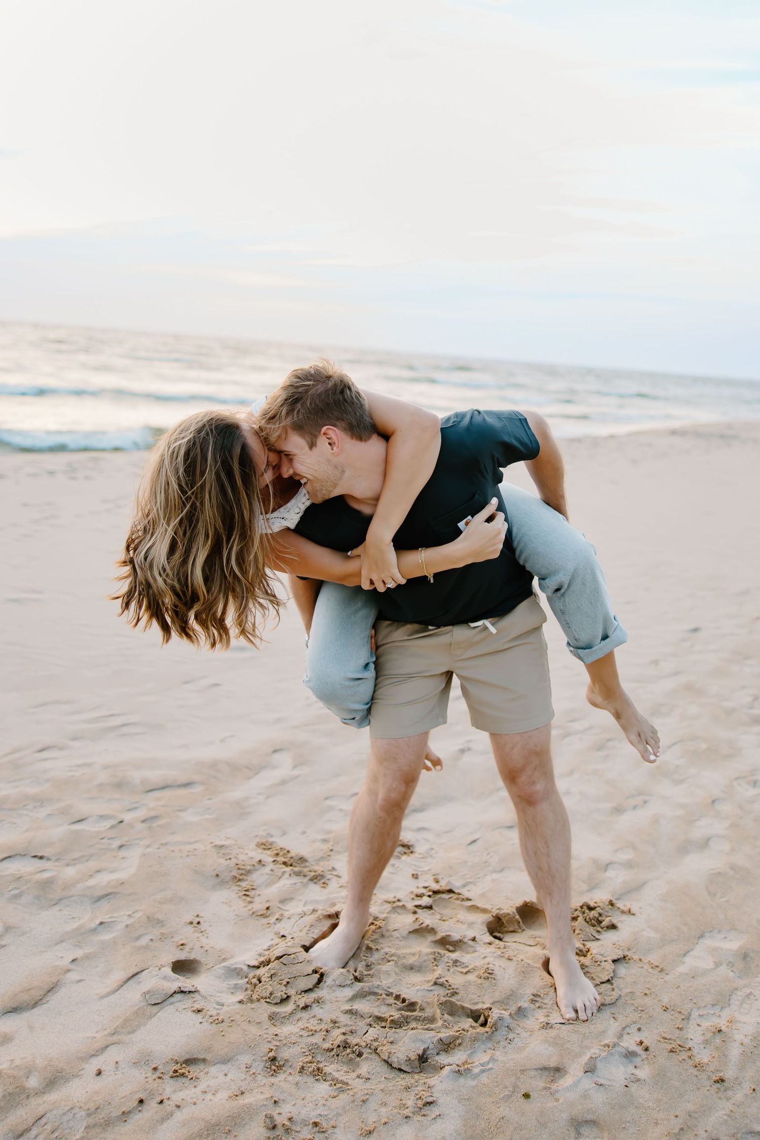 Playful couple embracing on a sandy beach at sunset.