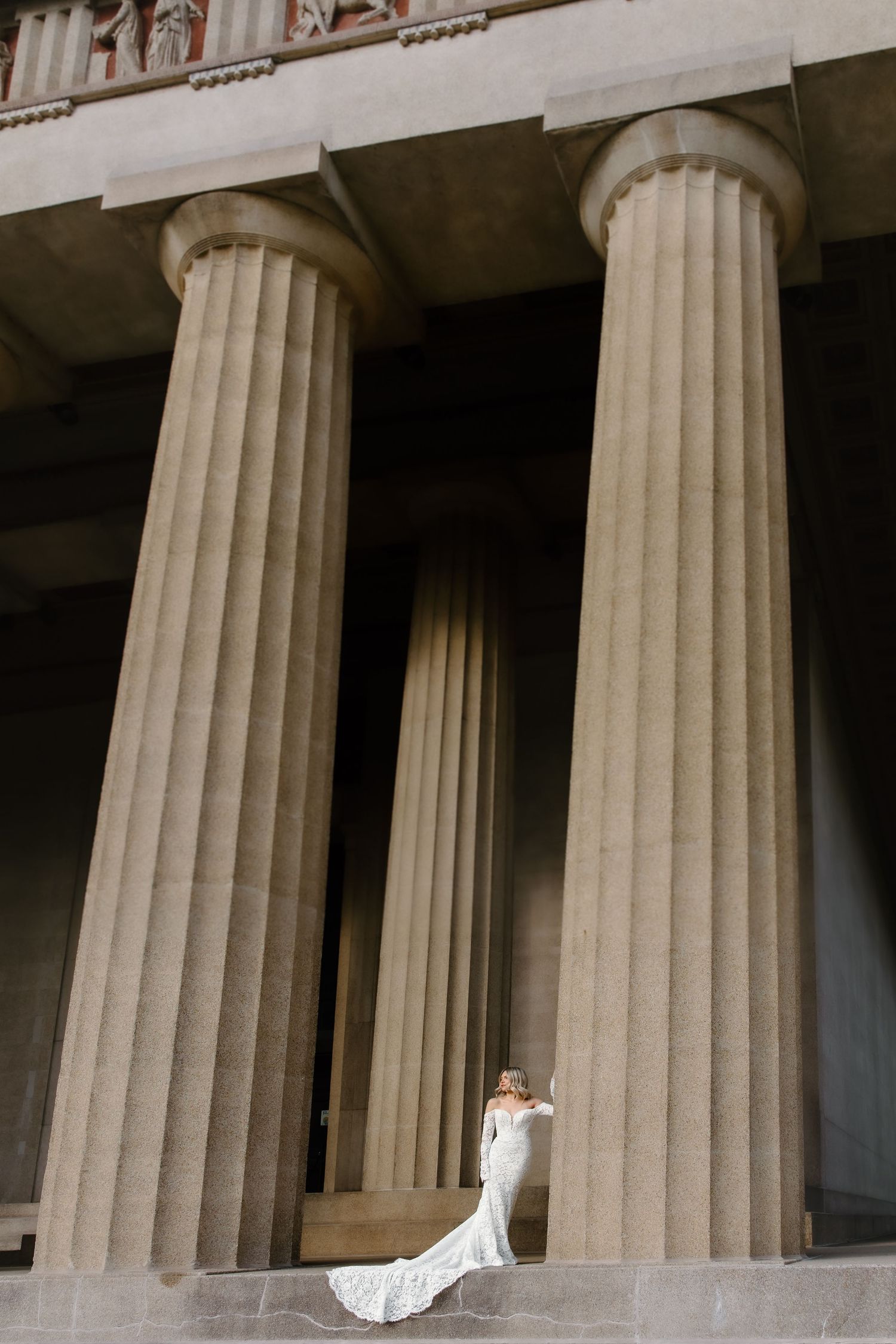 Bride in white gown poses between large neoclassical columns at the Parthenon in Nashville, Tennessee.