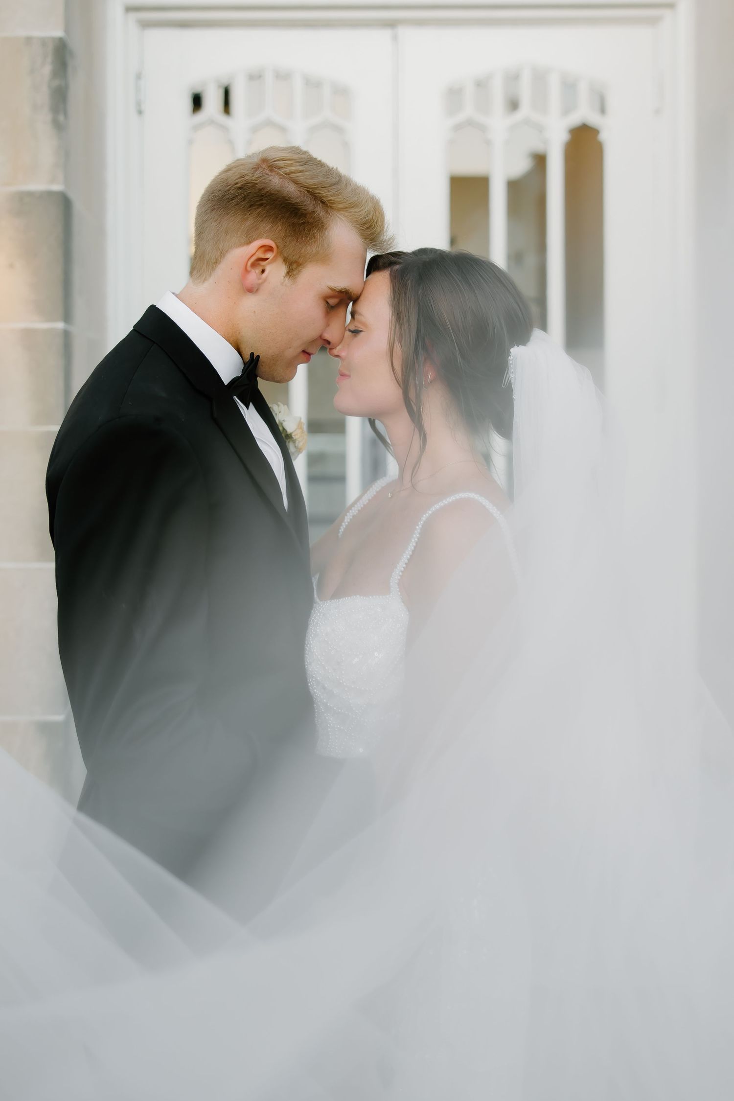 Ethereal indoor wedding portraits with soft natural light streaming through white curtains.
