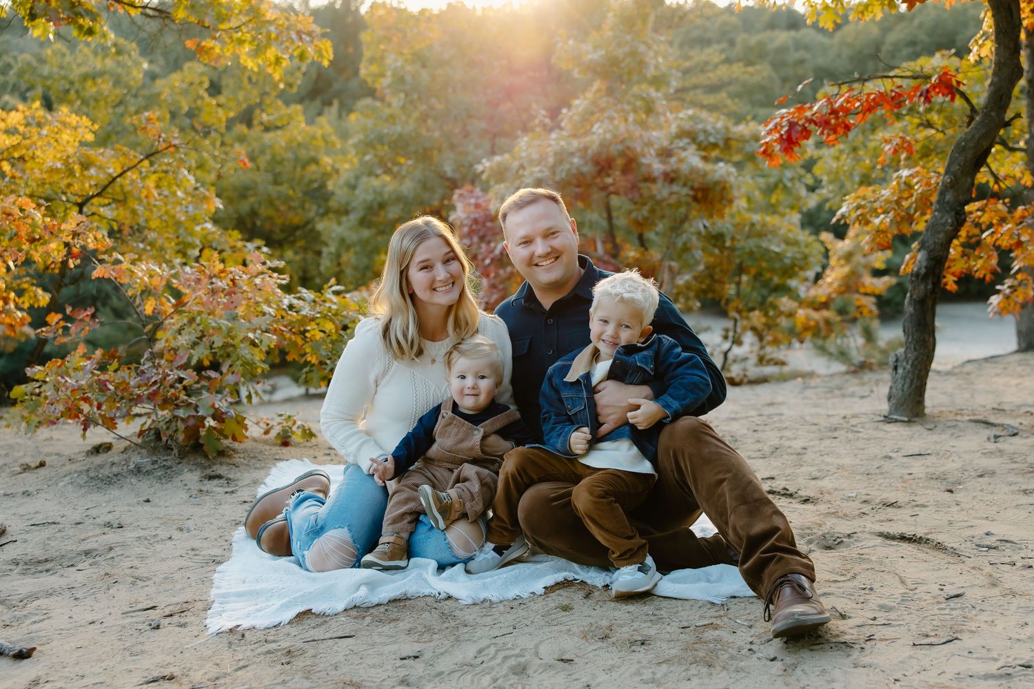 A group sits together on a blanket during sunset with fall colors in the background.