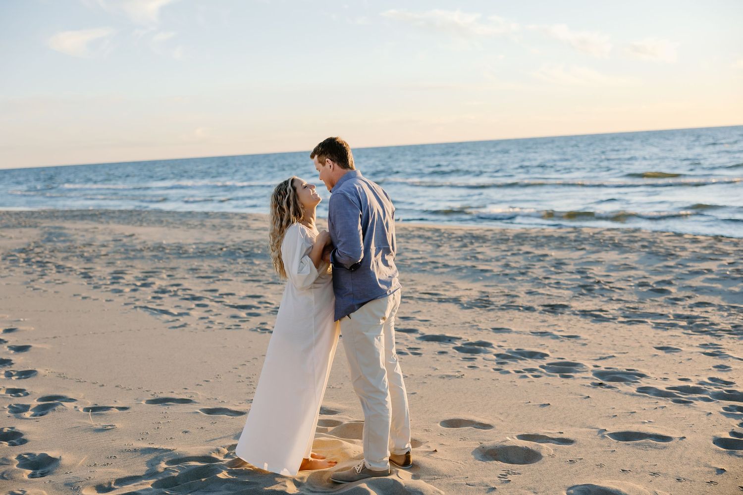 A romantic couple walks along a sandy beach at sunset holding hands by the ocean waves.