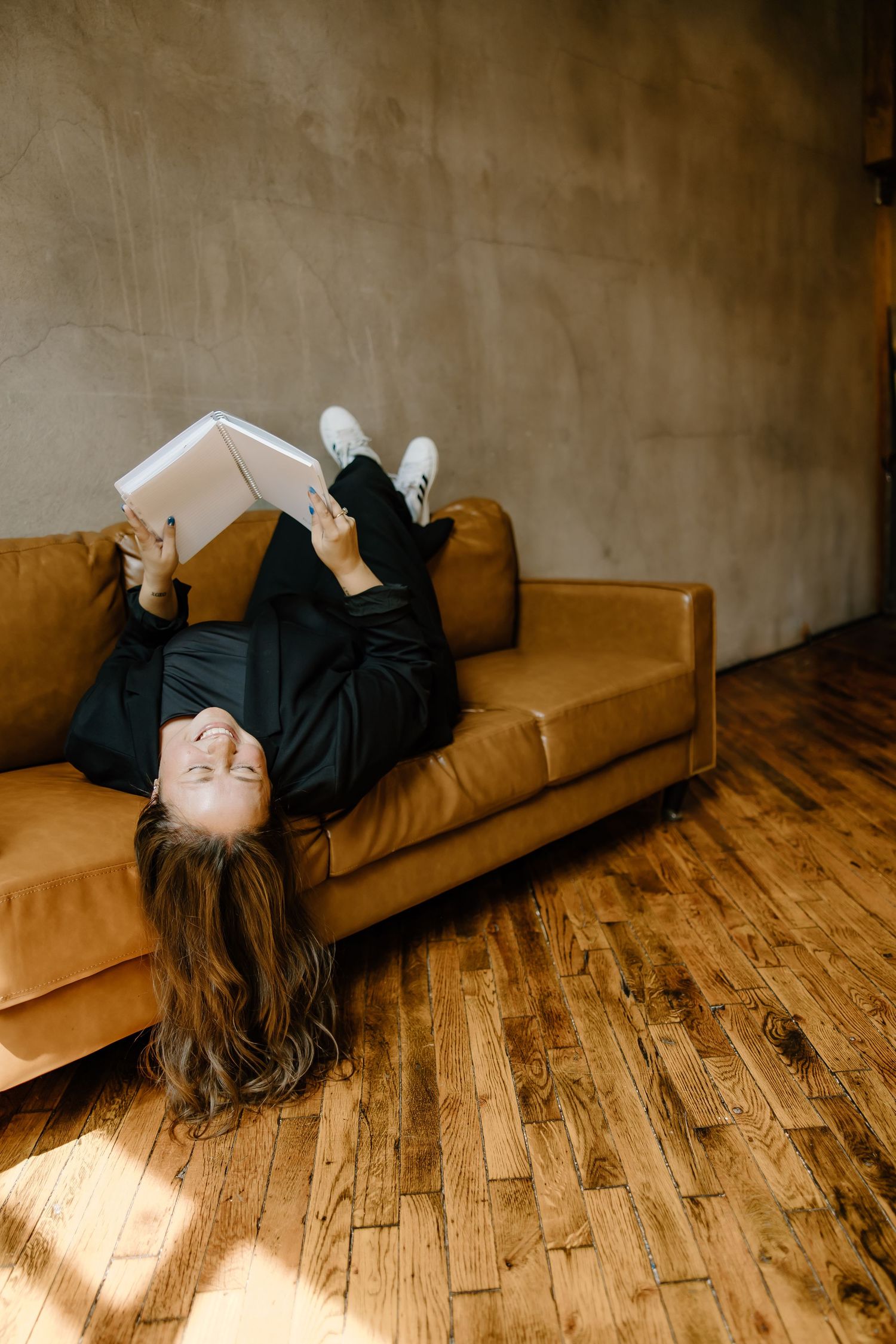 Playful photo of person lying upside down on tan leather couch while reading.