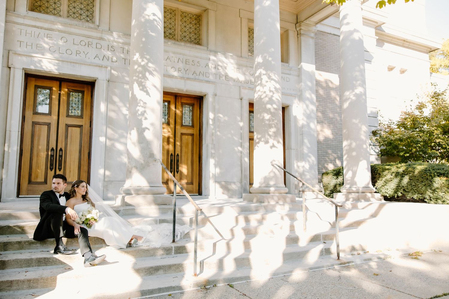 Elegant white building exterior with multiple wooden doors and columns casting dramatic shadows.