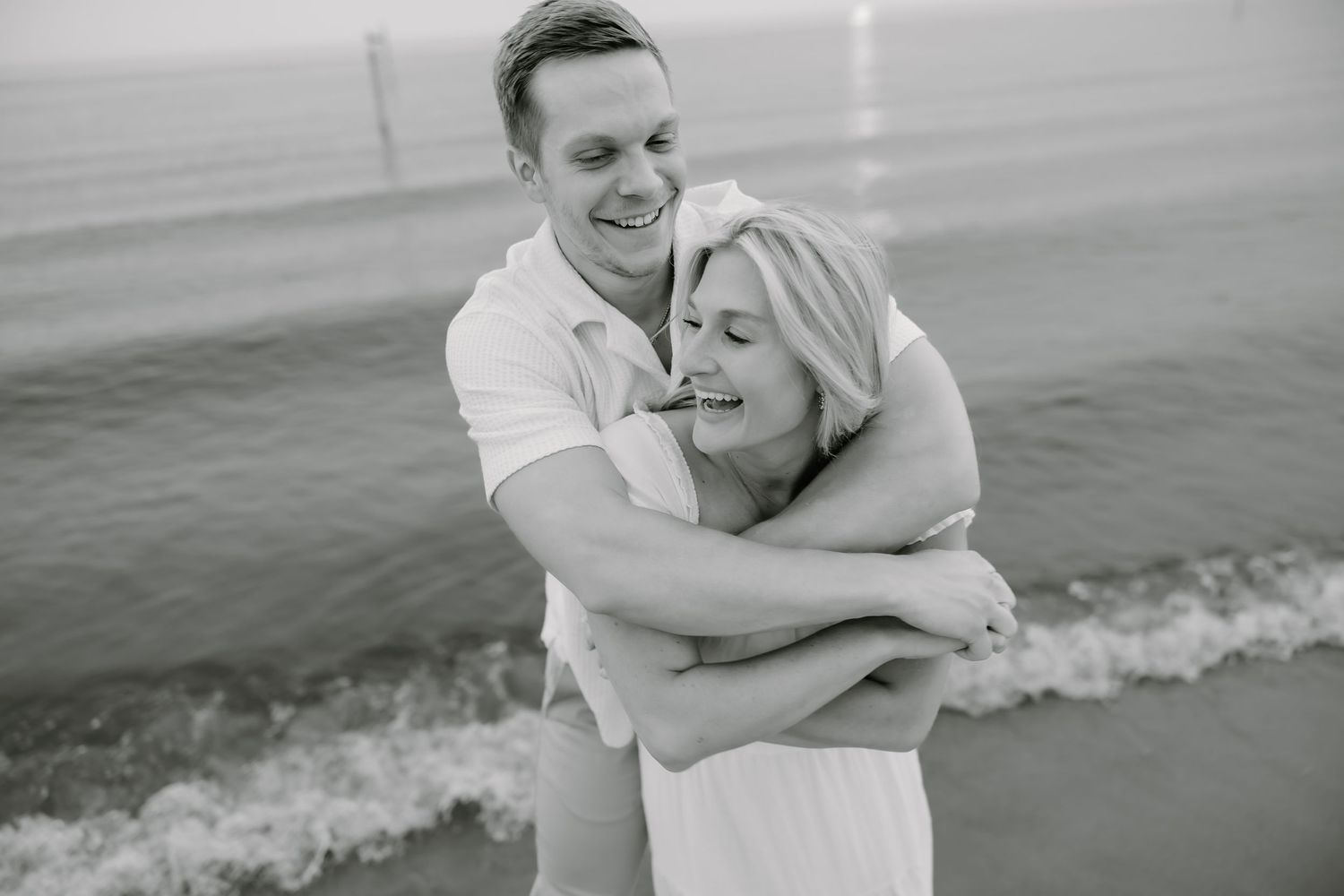 Black and white beach photo of joyful embrace by the ocean waves.