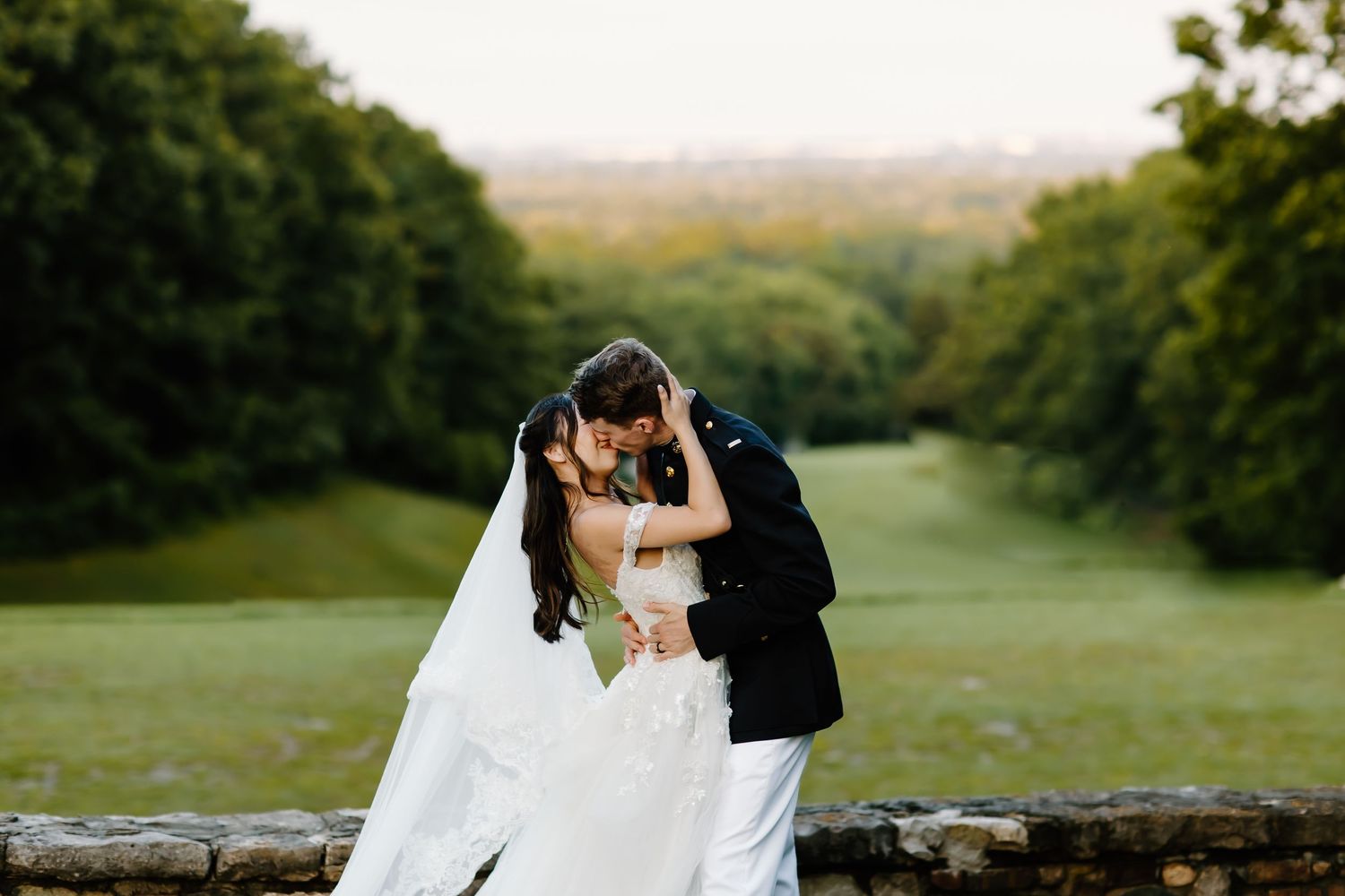Newlyweds embrace against a scenic hilltop backdrop during golden hour.