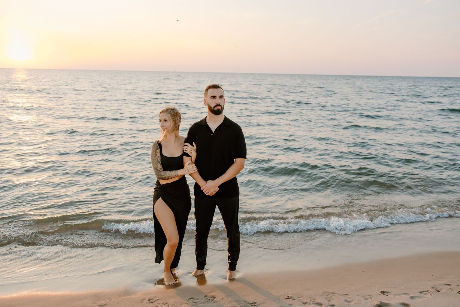 Couple strolling along beach at sunset with waves gently rolling in.