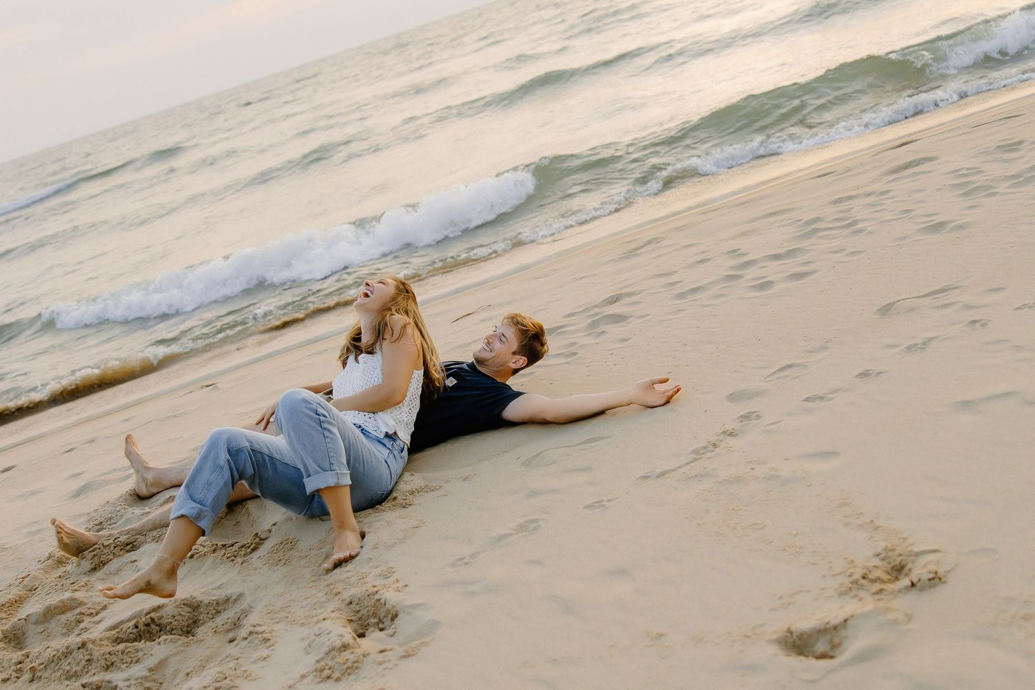 Couple lying playfully on a sandy beach at sunset.