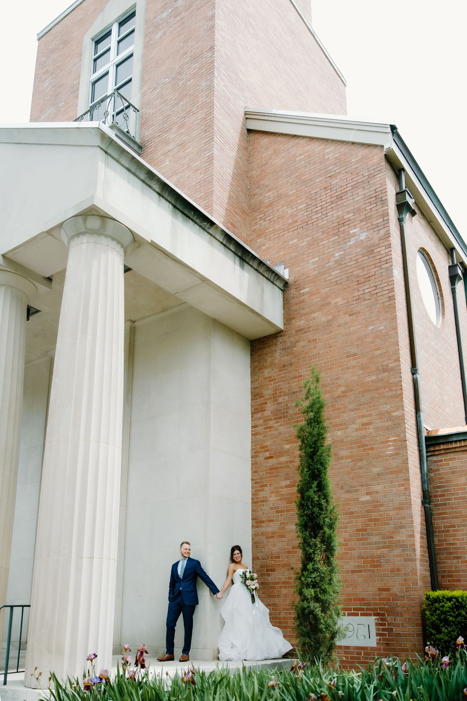 A classic brick church exterior with white columns and a couple standing on the steps.