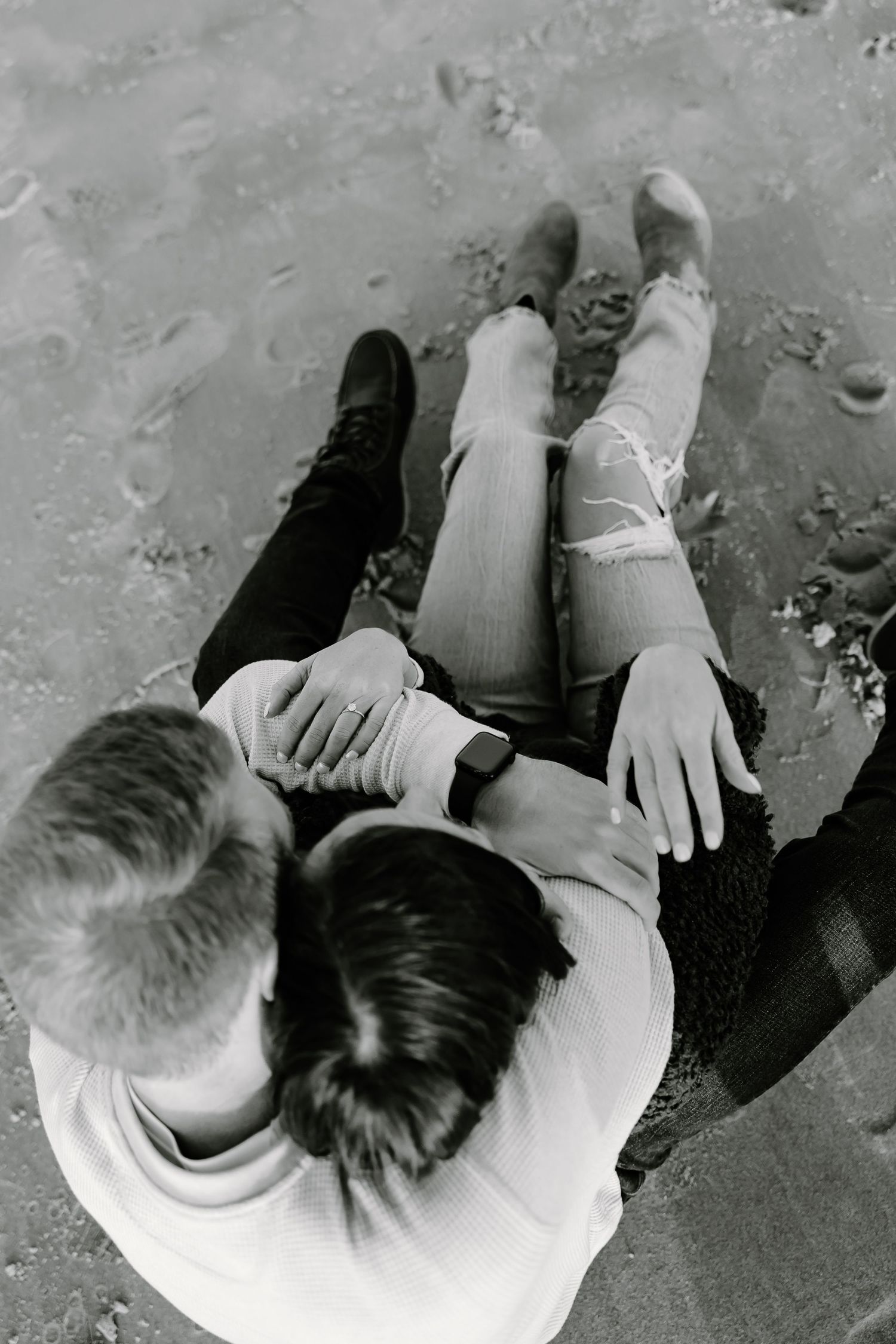 Overhead view of two people sitting close together on concrete.
