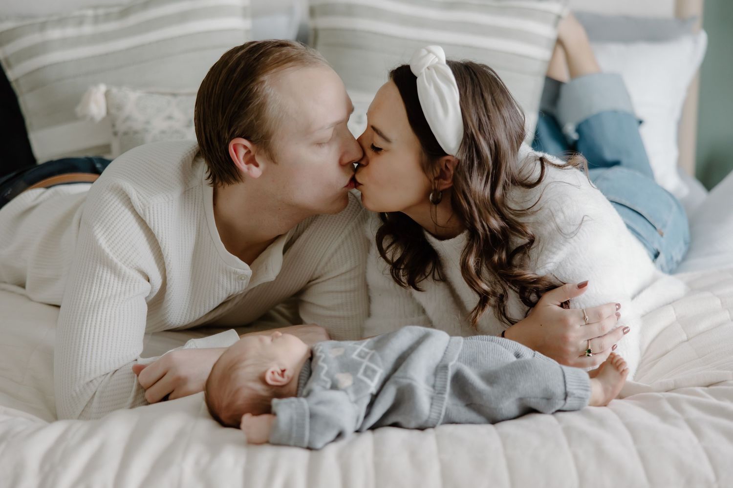 A tender moment shared between a couple lying on white bedding in soft natural light.