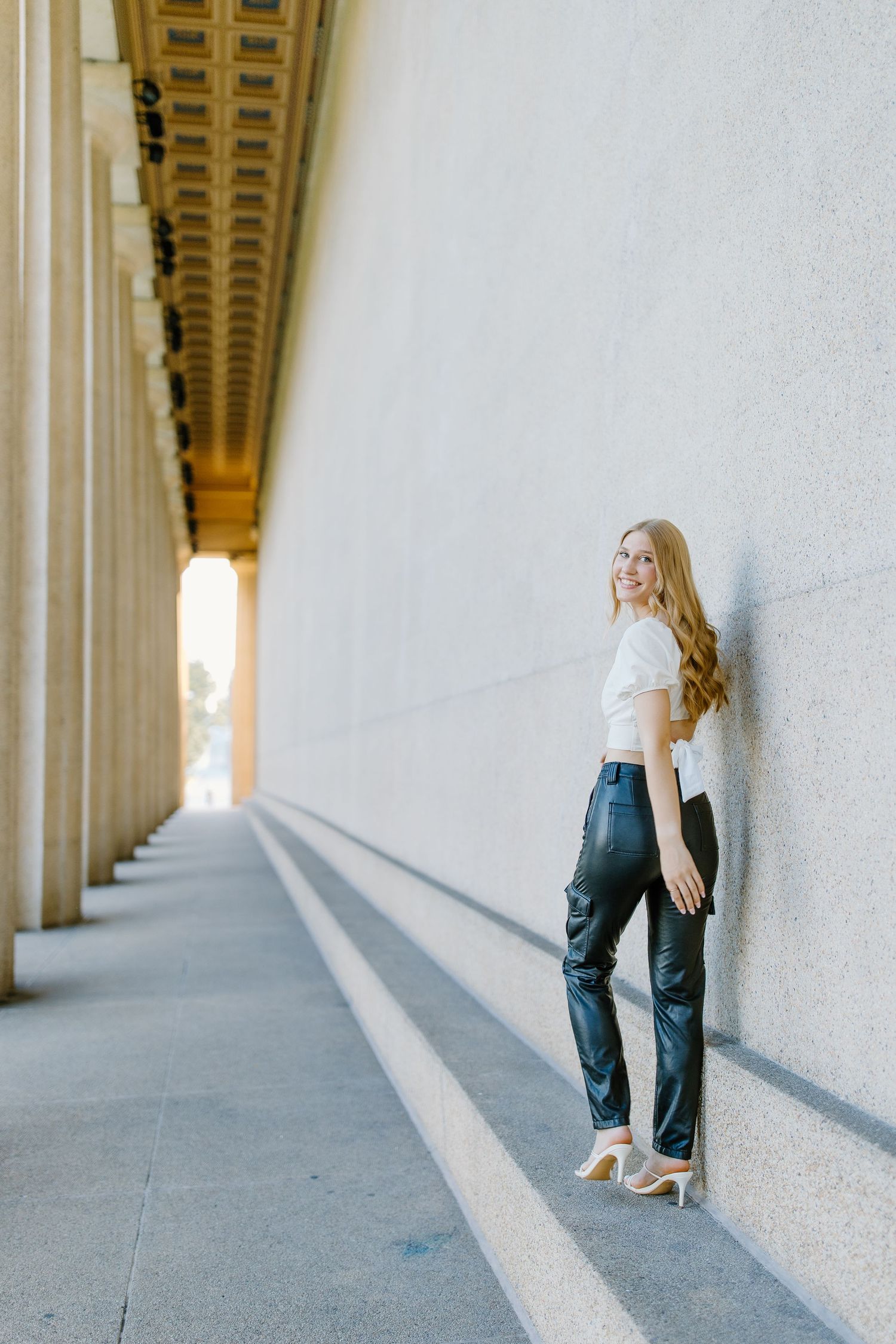 Person posing between classical white columns in an architectural corridor.
