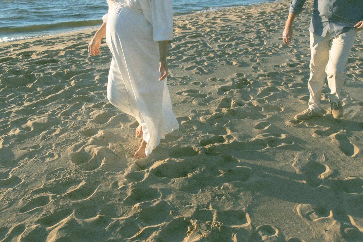 Couple walking hand in hand on a beach with waves crashing nearby.