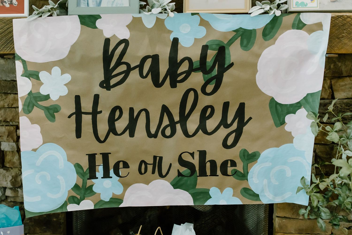 Decorative white floral and greenery wedding banners with names hang against a rustic wooden wall backdrop.