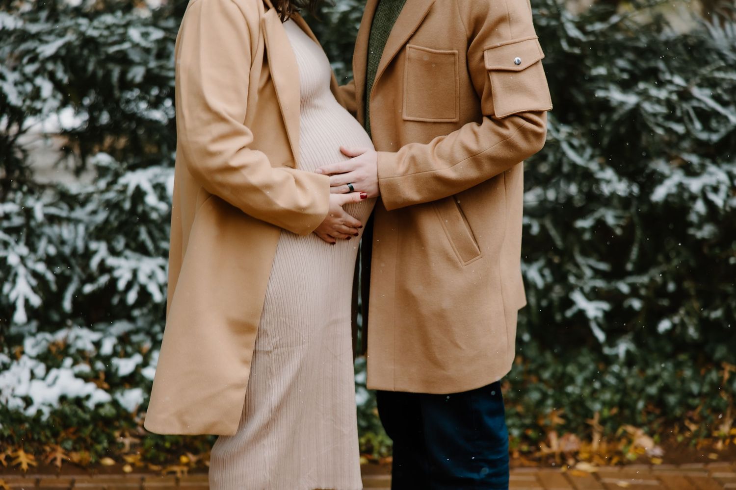 Winter maternity session featuring a woman in a beige coat and white dress.