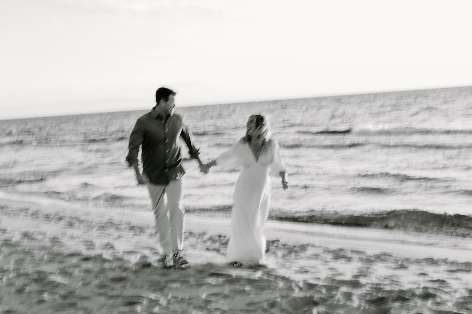 A couple walks hand in hand along a misty beach shoreline at sunset creating a romantic silhouette against the waves.