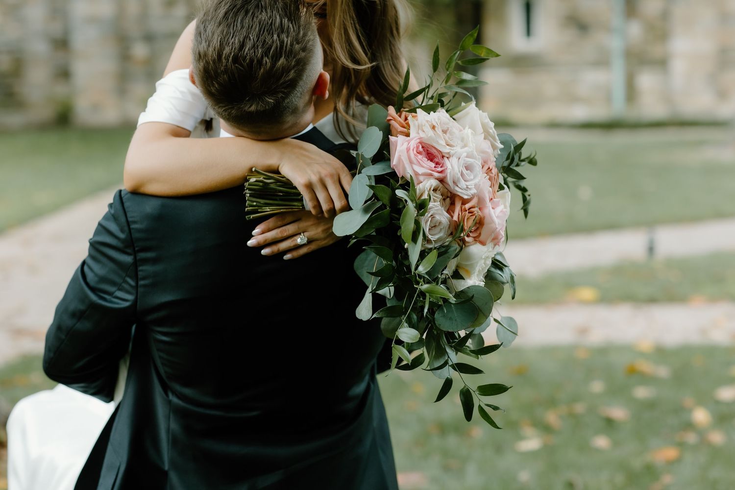 Elegant wedding couple embracing with pink floral bouquet.
