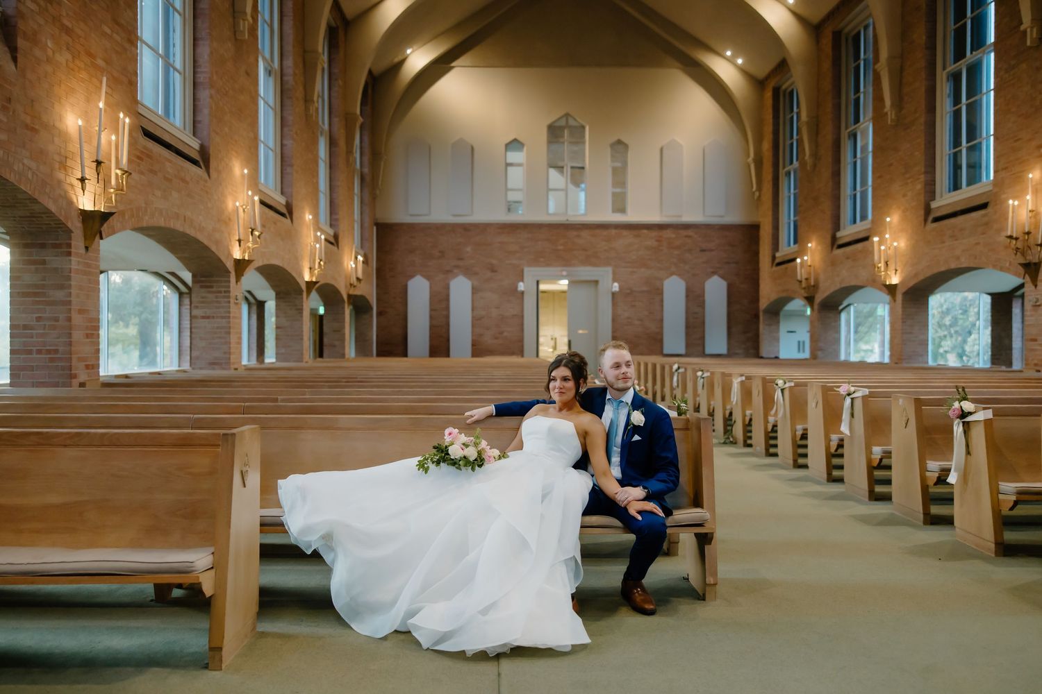 Elegant wedding couple dancing in a grand church hall with dramatic lighting and wooden columns.