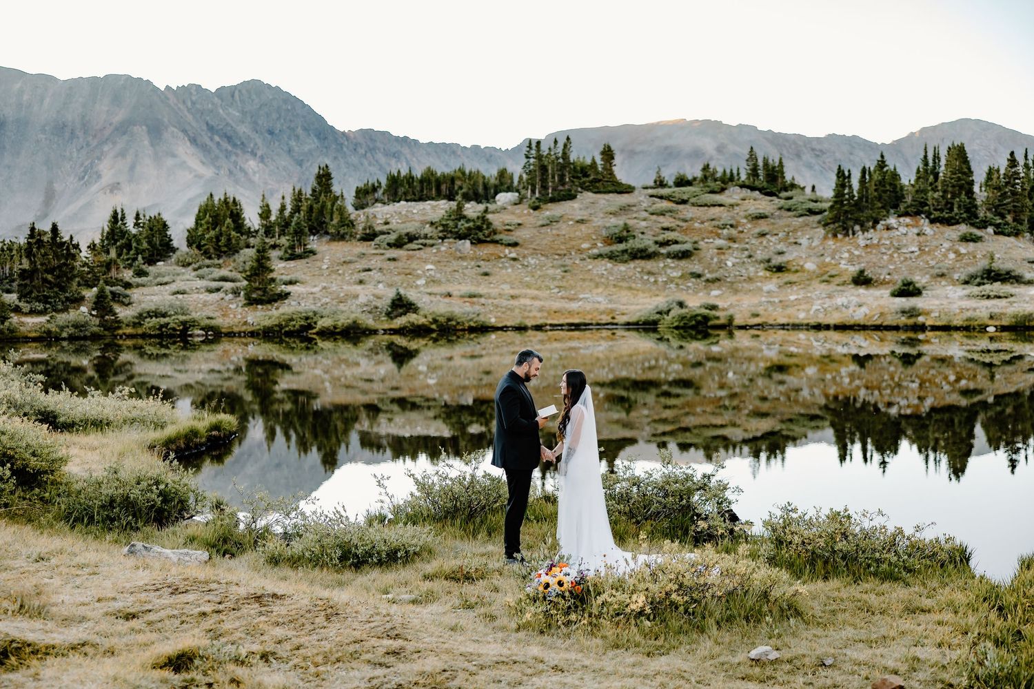 Wedding couple poses against stunning mountain lake landscape in panoramic view.