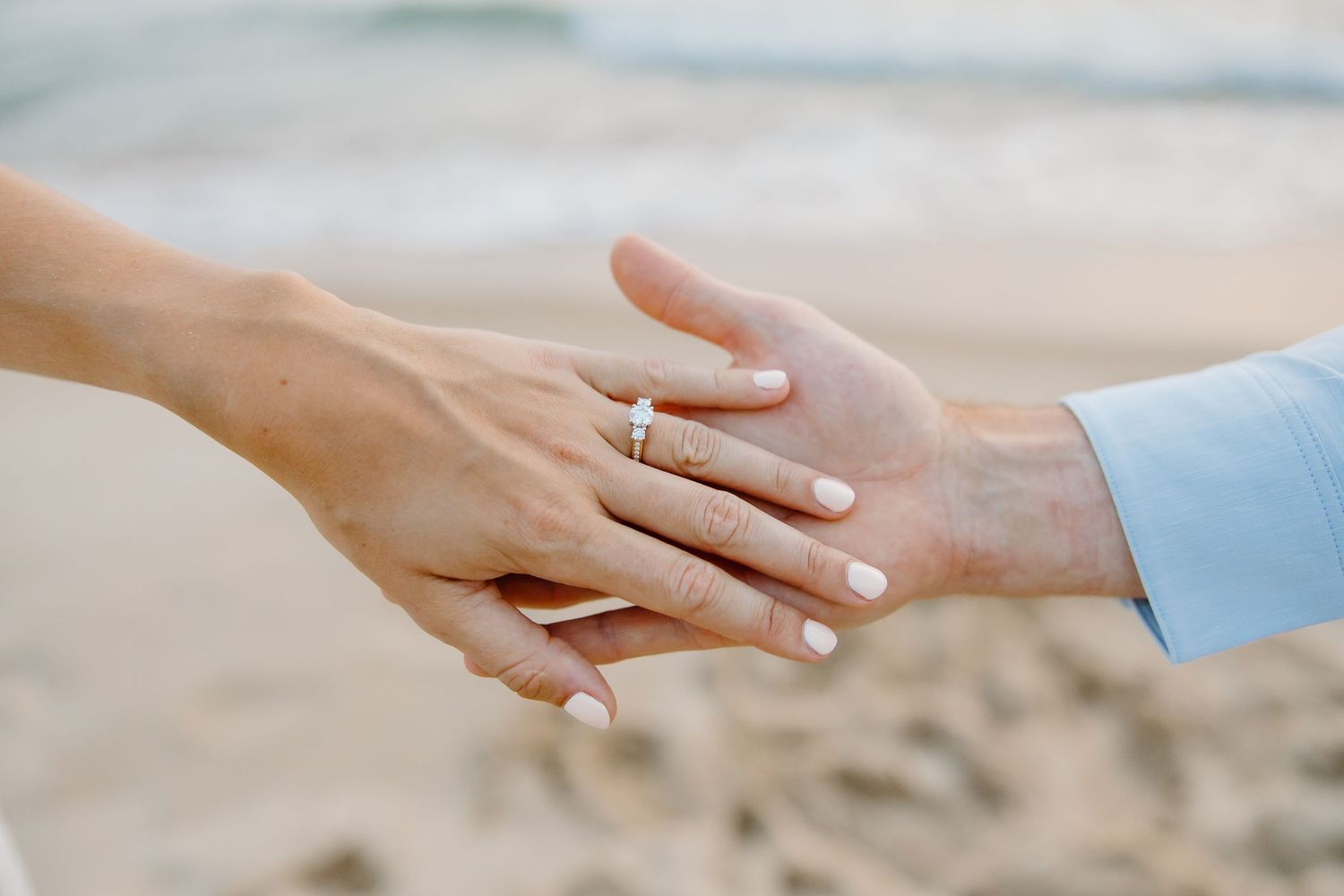 Hands with engagement ring touching against beach background.